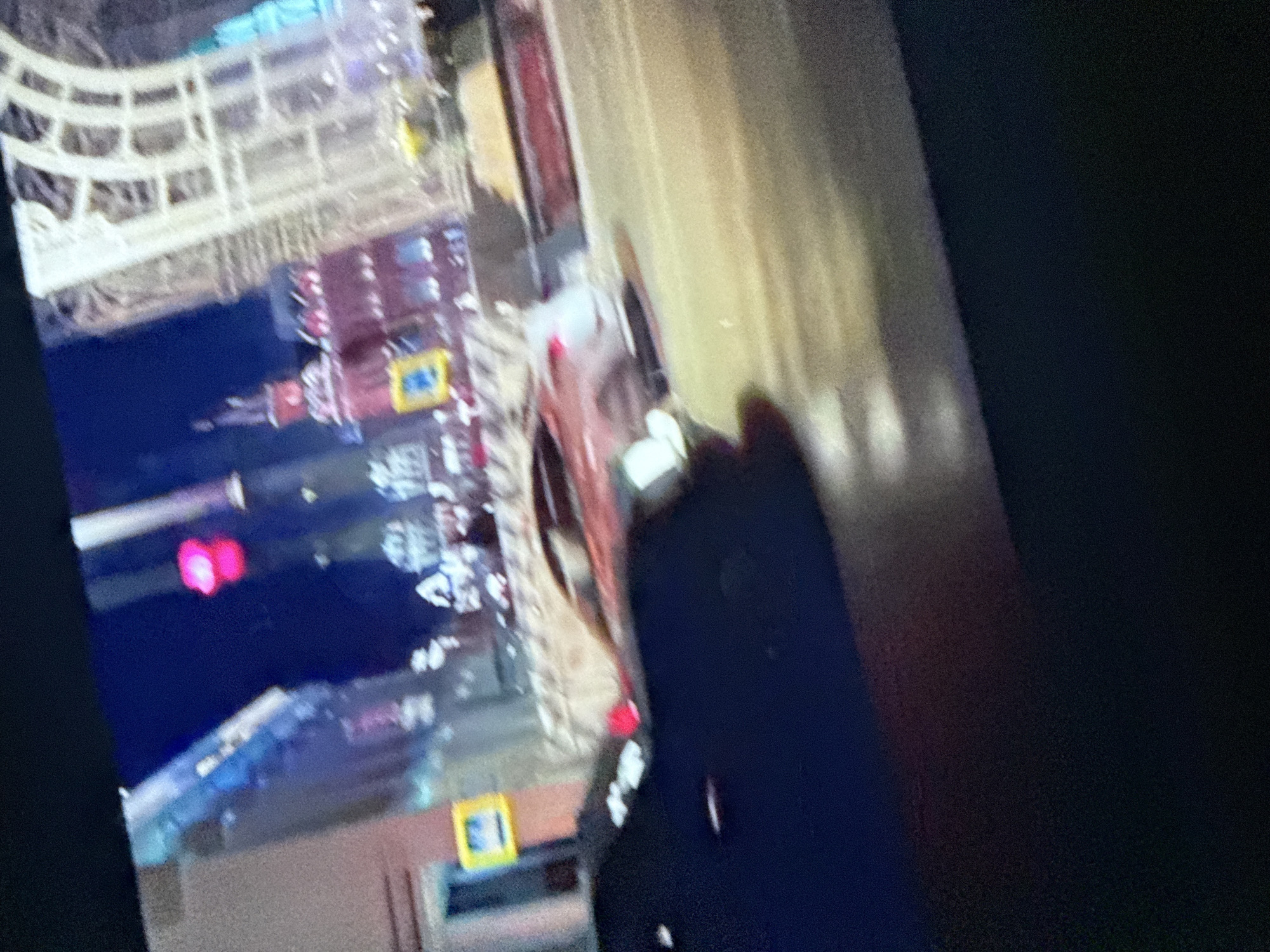 The image shows a blurry view of what appears to be a cityscape. There are building structures and possibly a bridge in the background. The presence of what might be a blue and red vehicle with lights further suggests an urban setting. However, image quality is poor, making definitive identification impossible. Mytishchi, Russia, cannot be confirmed, and details regarding people, subjects, objects, actions, interactions, and the environment cannot be elaborated upon due to the limited information available.