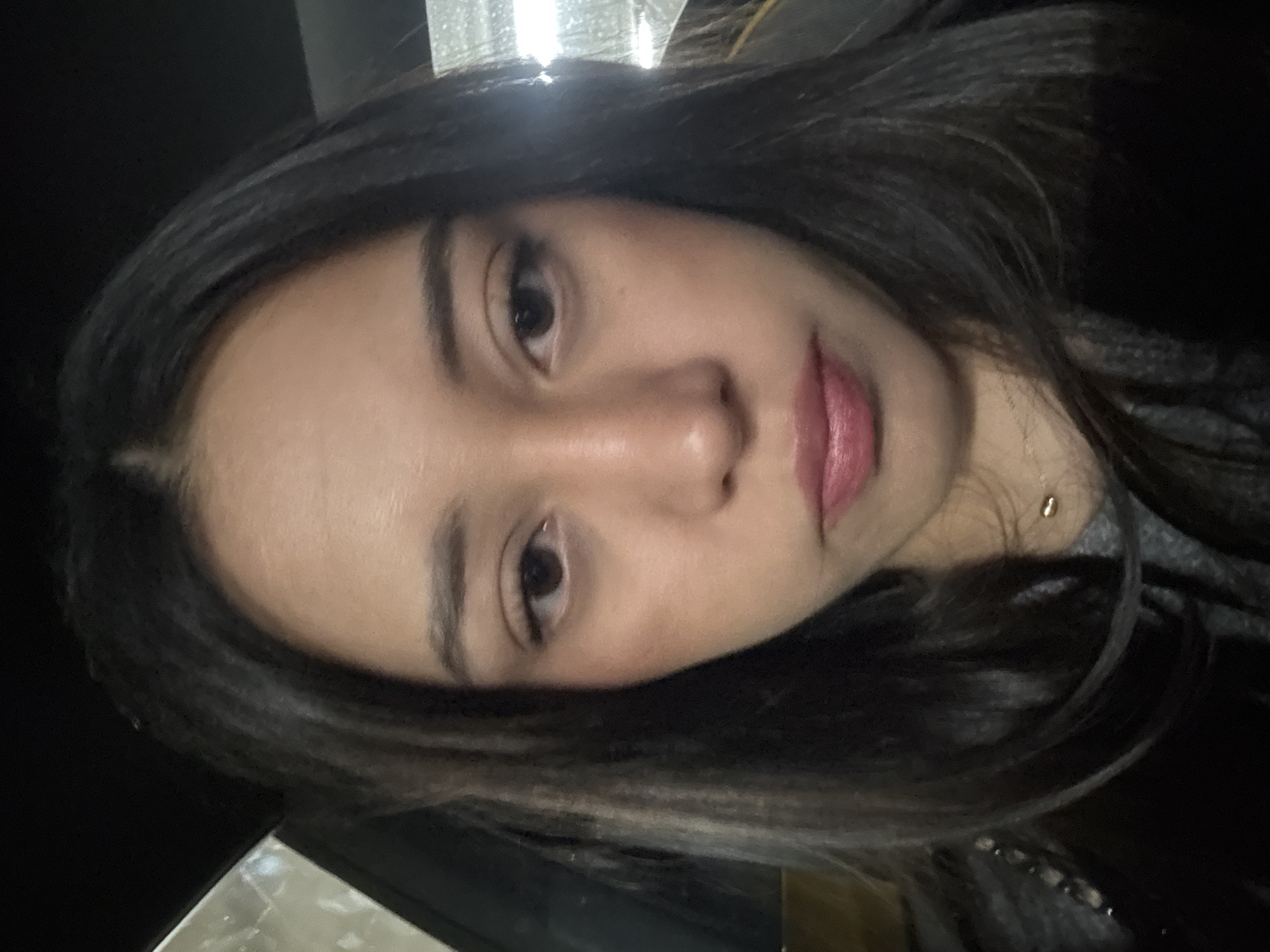 A close-up, rotated image shows a young woman with dark hair. She has light skin, dark eyes, and pink lips. A gold necklace is visible at her neck. The background appears dark, possibly indoors. It is not possible to determine the location in Mexico City, Mexico, from the image.