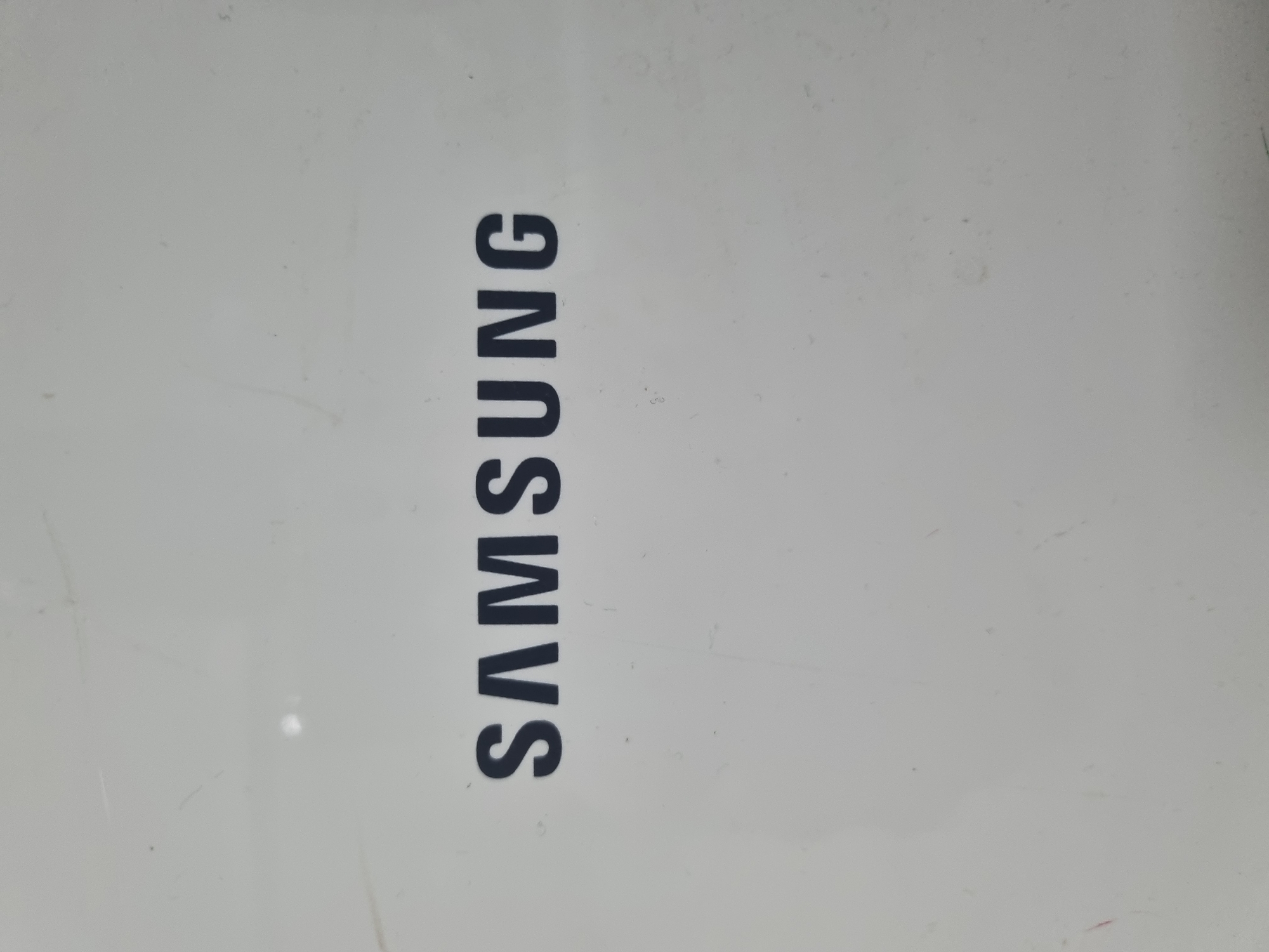 The image shows the SAMSUNG logo printed in dark blue on a white surface. The surface appears to be a device or an appliance. The logo is centered horizontally and vertically in the frame. The surface has some minor scratches and smudges, indicating it is not pristine. There are no people or other objects visible in the image. The location in Hwaseong-si, South Korea, is not discernible from the image itself; this information would be external to the visual content.