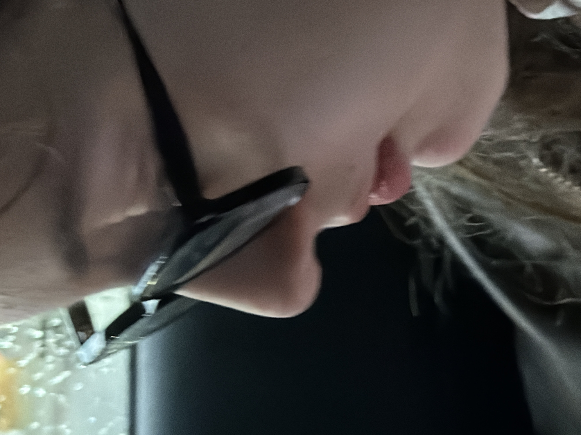 A close-up shot from a low angle shows a person's face, including the chin, lips, and part of the cheek. The person is wearing glasses. The background is dark. The location is not discernible from the given information.