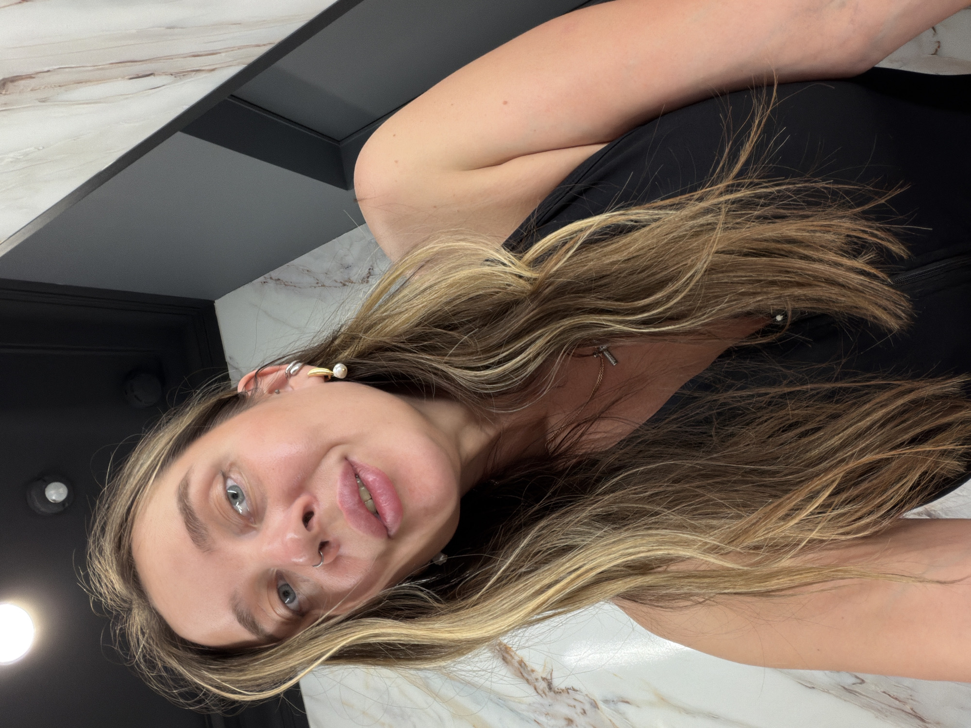 A blonde-haired woman with blue eyes is looking at the camera. She is wearing a black top. The background consists of a marble countertop and dark-colored cabinetry. The photo does not contain information about the city of Moscow, Russia.