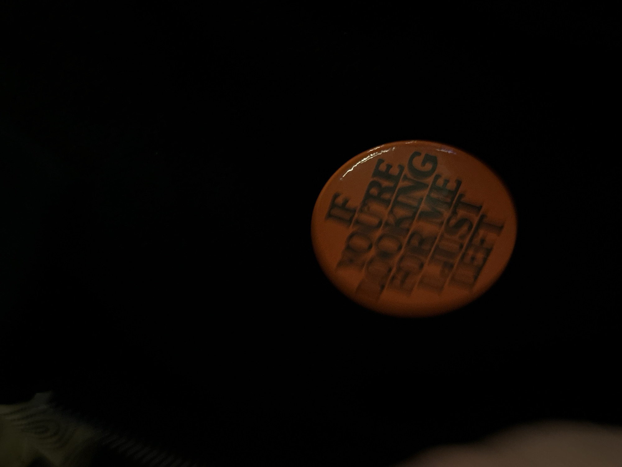 An orange button with black text reading "IF YOU'RE LOOKING FOR ME I JUST LEFT" is positioned on a dark surface. Due to the lack of details, location in London and specific actions and interactions cannot be determined.