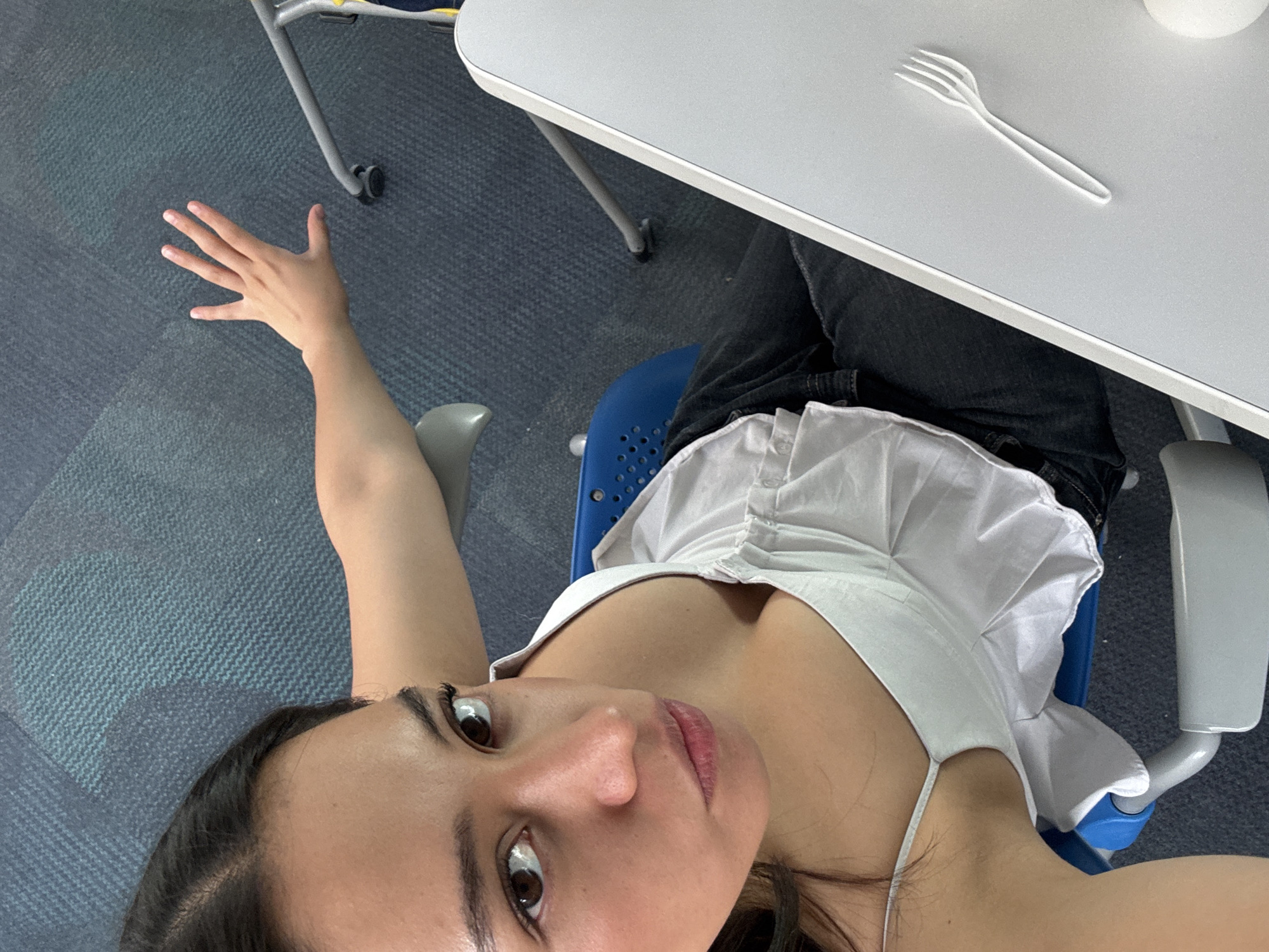 A woman is seated at a desk with a white plastic fork on top. She wears a white top and dark jeans. She has her left arm extended out to the side. The floor is covered in blue carpet tiles. The photograph appears to have been taken indoors. There is no evidence to suggest the location is in Puebla, Mexico.