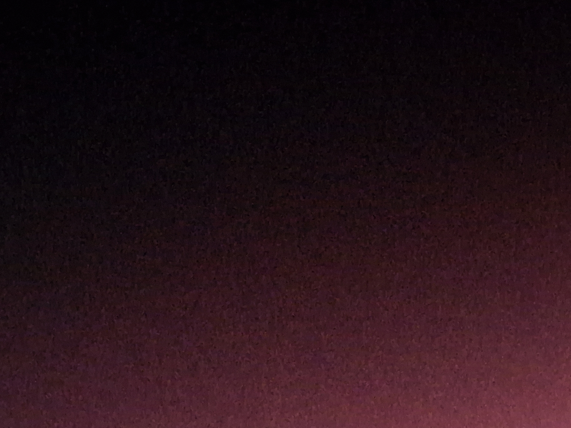The image displays a dark, textured background with a gradient effect, transitioning from a deep maroon or burgundy at the top to a near-black at the bottom. The texture appears to be granular, resembling fine speckles or a coarse fabric. There are no discernible objects, people, or environmental features visible in the image. Therefore, it is not possible to determine any specific location within the city of Kokshetau, Kazakhstan, or any details about a scene.