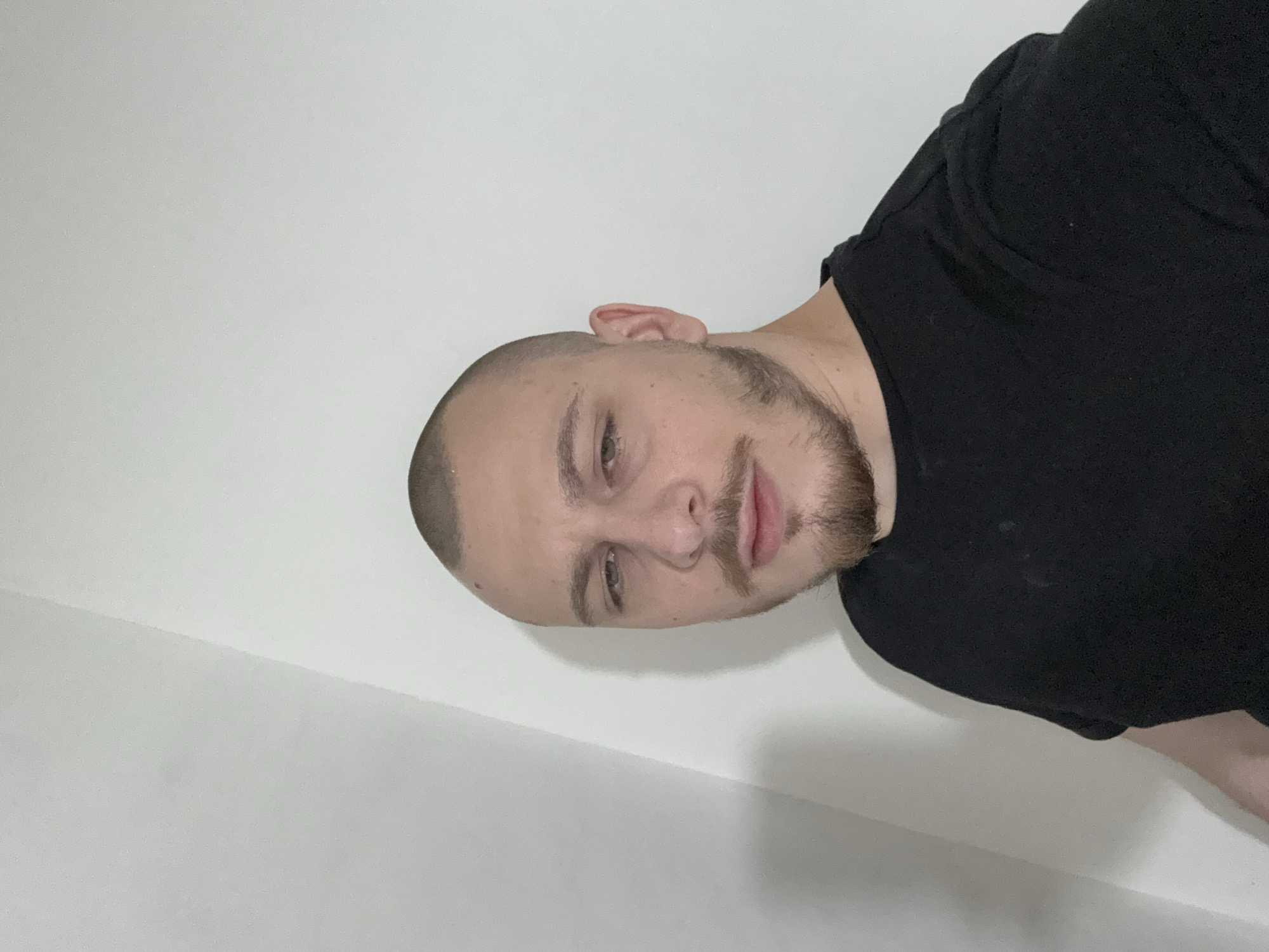 A man with a shaved head and a beard is looking into the camera. He is wearing a black t-shirt. The background is a plain white wall. There is no indication of a location, nor a city, nor of Stara Zagora, Bulgaria.