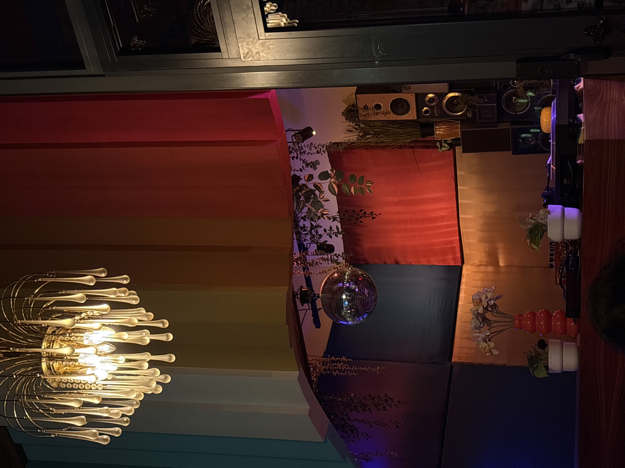 The image shows an interior shot of a room with colorful wall panels ranging from red to blue. A large, ornate chandelier hangs on the left side. A disco ball is centrally positioned. There are various decorations on the walls, including plants, speakers, and vases.
Without additional information, it is impossible to confirm the location of the city of Belgrade, Serbia.