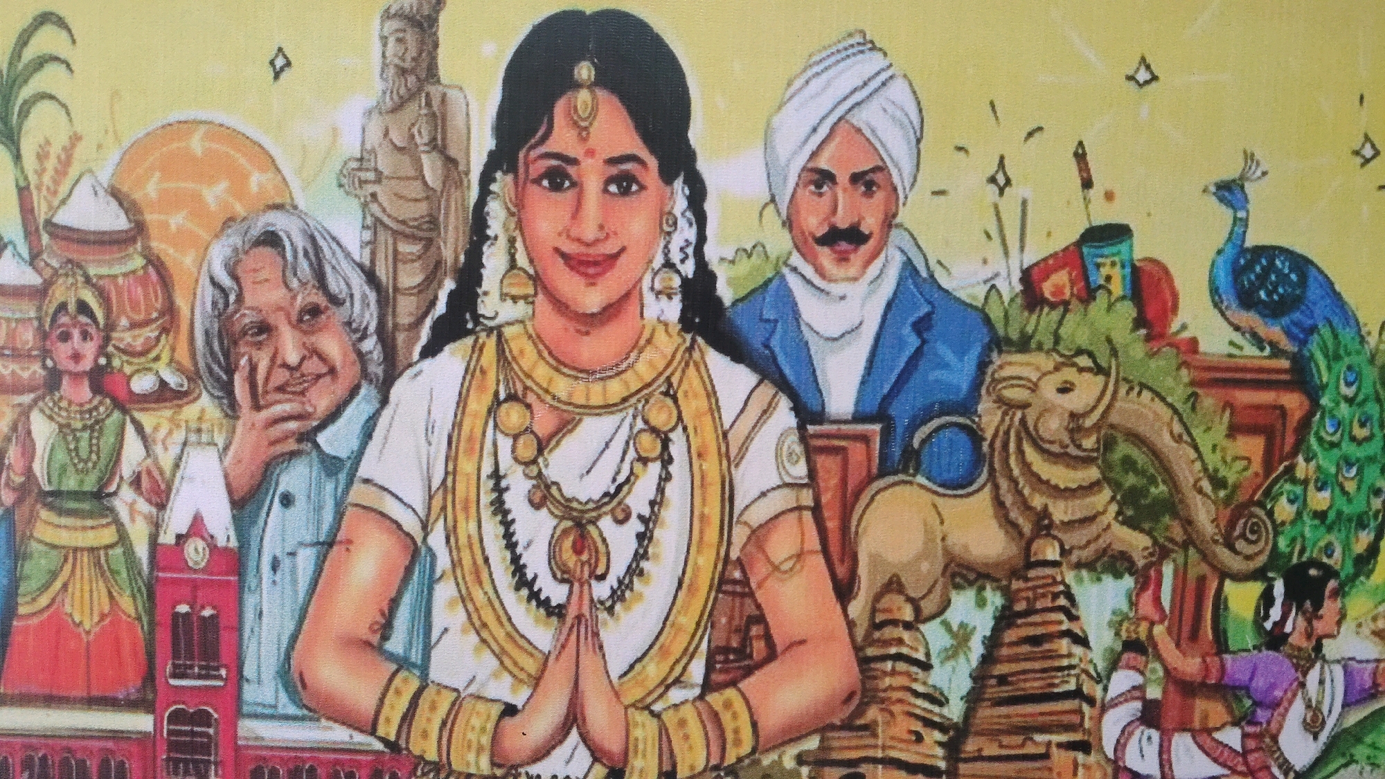 The image is a colorful, stylized illustration depicting a vibrant cultural scene, likely a mural or artwork. In the foreground, a young woman with traditional Indian attire and jewelry, including a white sari with gold trim and bangles, offers a Namaste greeting with her hands pressed together. To her left, a smiling elderly man with gray hair, resembling a prominent figure like Dr. A.P.J. Abdul Kalam, is depicted with his hand near his chin. Behind the woman, a man in a blue jacket and white turban with a mustache is visible. The background is a collage of cultural elements. To the left, a woman in green and red traditional attire stands near harvest imagery like sugarcane and pots. A prominent red building with clock towers, resembling the Perundurai Railway Station, is featured. Further back, a stone statue of a bearded figure and various architectural structures like tiered pagodas are present. On the right, a peacock stands near fireworks and traditional Indian motifs. A carved sculpture resembling a lion-elephant hybrid rests on a tiered base, and a woman in a purple and white outfit performs a yoga pose. The overall atmosphere is celebratory and rich in cultural symbolism.
