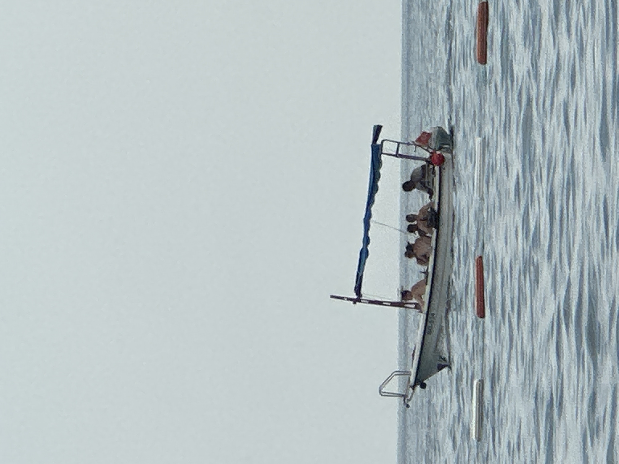 A motorboat with an awning is on the water. Five people are on the boat. The sky is overcast and the water is calm. Two buoys are visible in the water in front of the boat. The boat has a registration number visible. This scene is in the waters off the coast of Boreti, Montenegro.