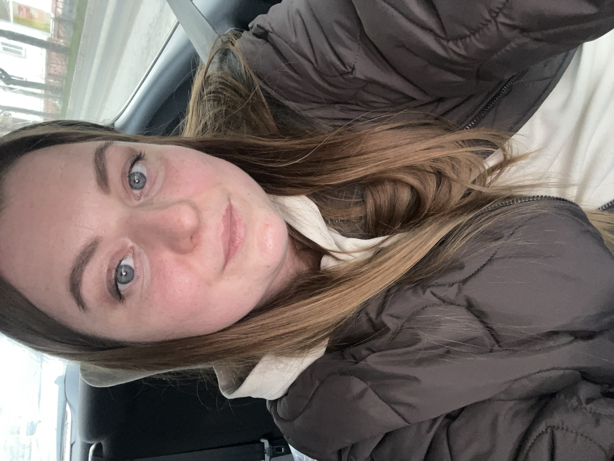 A fair-skinned woman with light brown hair and blue eyes is looking at the camera. She appears to be in the passenger seat of a car, wearing a brown quilted jacket over a light-colored top. The scene outside the car window is indistinct. The location, Klin, Russia, is not discernible from this image alone. There are no discernible actions or interactions in the image beyond the woman posing for the photo.