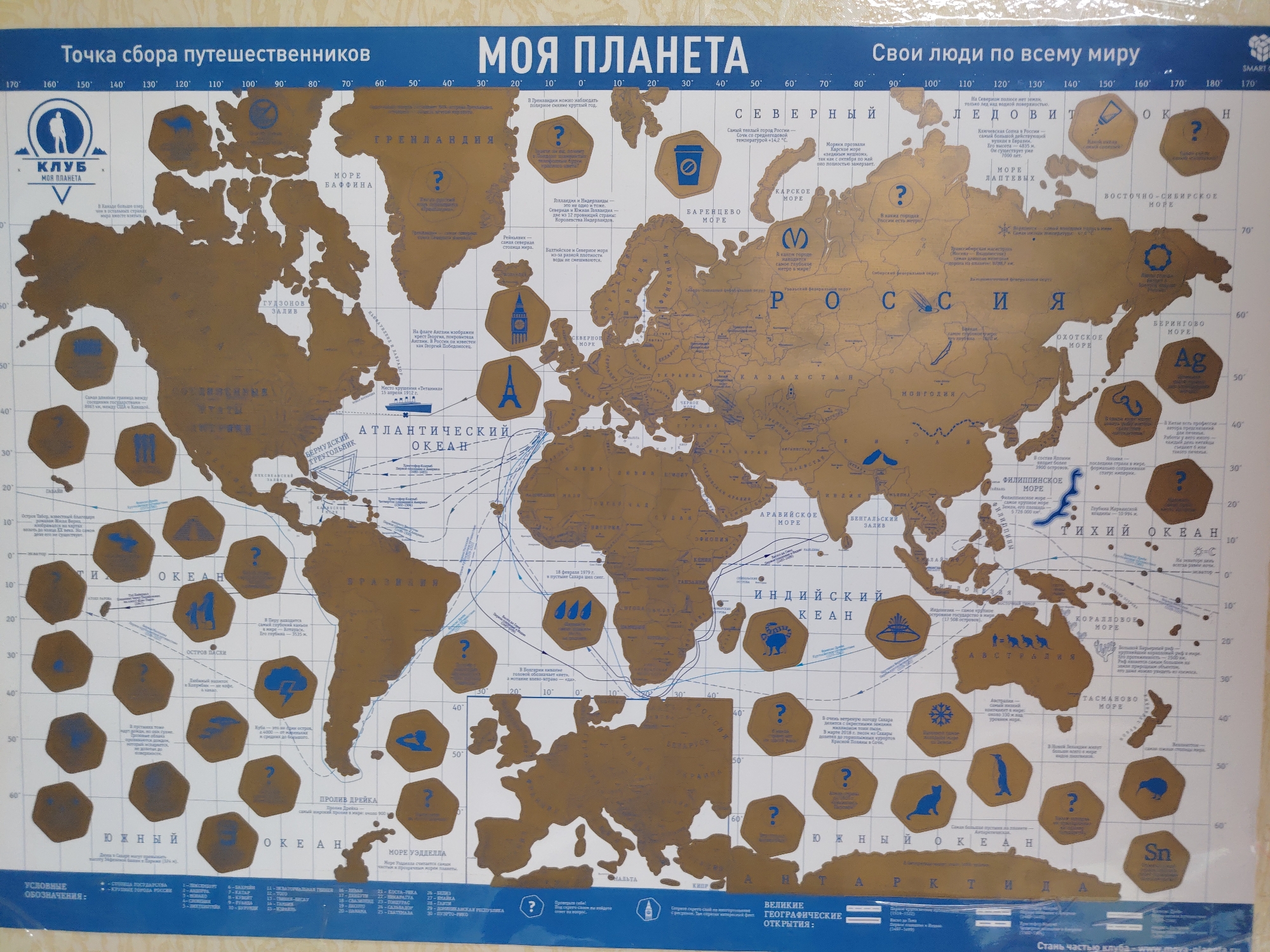 The image is a world map displaying various geographic and cultural facts. It is labeled "Моя Планета" (My Planet) and "Точка сбора путешественников" (Travelers' Gathering Point) at the top left. The map shows continents, oceans, and notable landmarks, accompanied by descriptive text in Russian. It contains icons and illustrations denoting cultural aspects, natural phenomena, and geographic features. The map has a coordinate system along the edges, indicating latitude and longitude. The bottom of the map includes a legend explaining the symbols and labels used. The city of Chaikovsky, Russia, is not discernible from the given image.