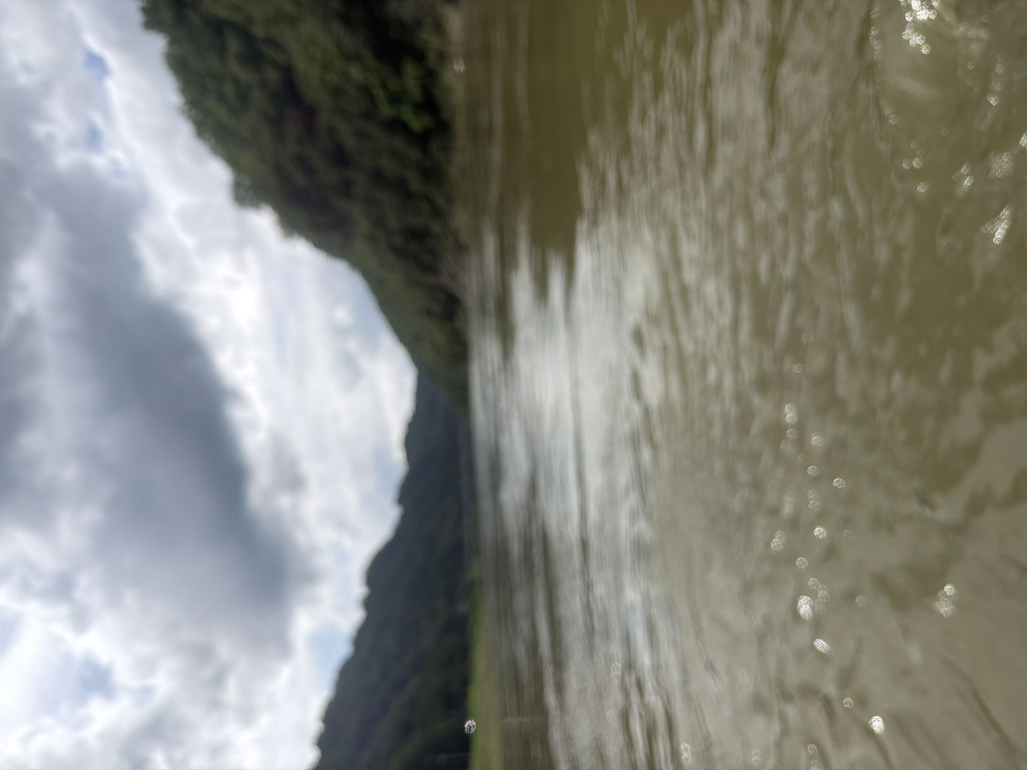 The image depicts a blurry, wide-angle view of a body of water, likely a river, with forested hills on either side. The water has a greenish-brown hue, and there are reflections of light on its surface, appearing as small, bright circles. The sky is overcast with dark, dramatic clouds. The scene suggests a natural, possibly remote, environment. The provided location of Seo-myeon, South Korea, indicates that this is a landscape image of that region. There are no discernible people, subjects, objects, or actions in the image due to its blurriness.