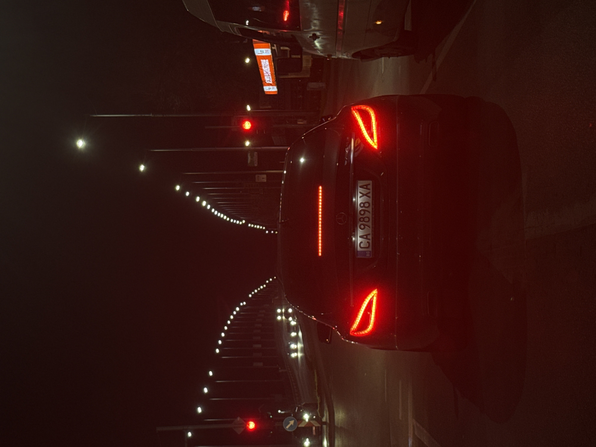 A nighttime scene in Plovdiv, Bulgaria, showing the rear of a dark-colored car with license plate "CA 9898 XA" stopped at a red traffic light. The location appears to be within a tunnel, as indicated by the rows of lights lining the tunnel walls. There is another vehicle visible partially above the car, also stopped. A roadside sign is visible above the car. The overall environment is dark, with artificial light illuminating the scene.