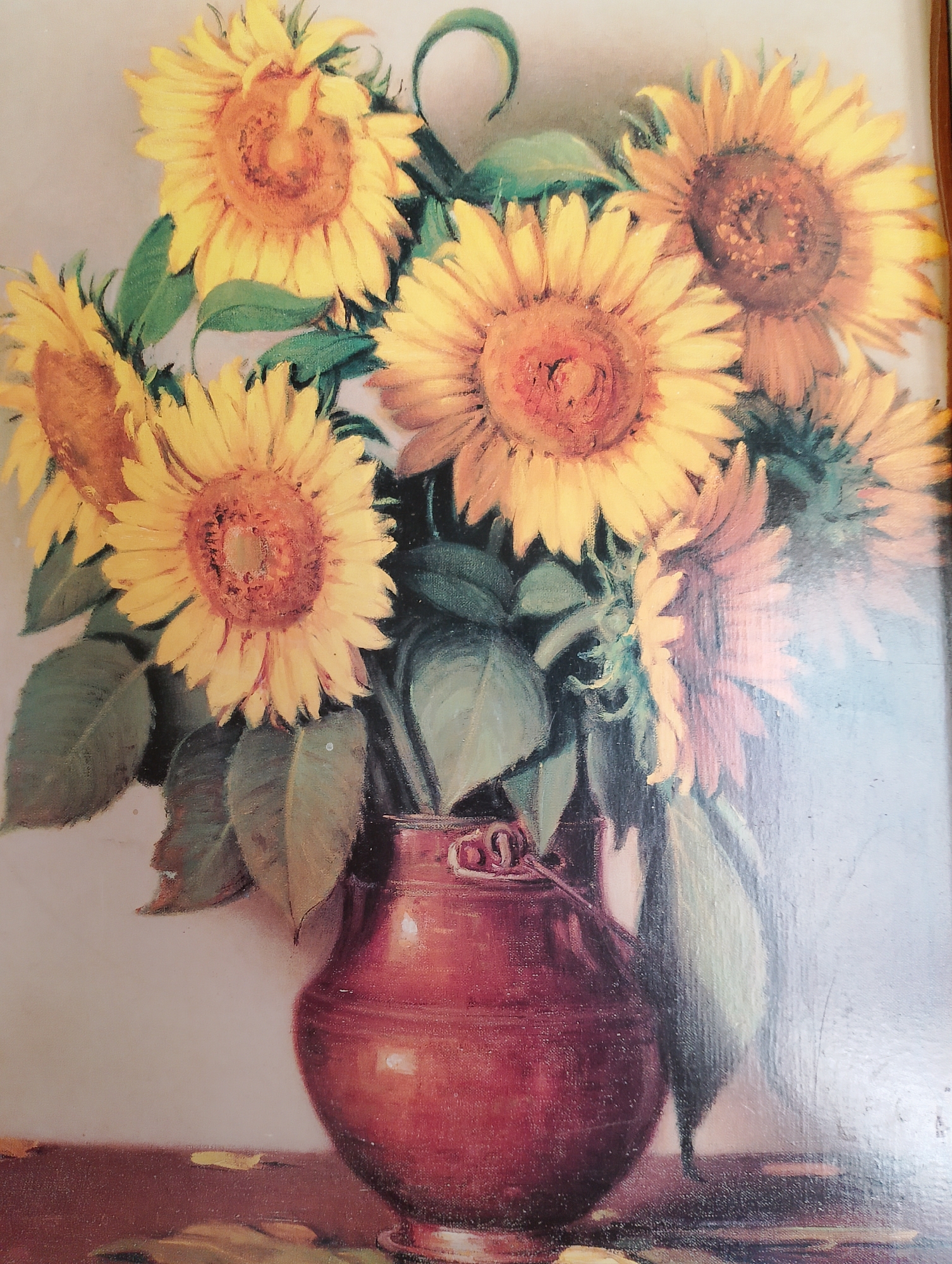 A still life oil painting depicts a bouquet of sunflowers in a deep red, ceramic vase. The sunflowers are vibrant yellow with prominent, dark brown centers, and are arranged artfully, with some facing forward and others slightly turned. Lush green leaves and stems complement the bright petals, creating a natural, organic feel. The vase is bulbous in shape with a slightly flared rim and two small, decorative handles. It rests on a dark, flat surface that appears to be a tabletop. Scattered on the surface are a few fallen sunflower petals, adding a touch of realism to the composition. The background is a soft, muted cream color, which allows the sunflowers and vase to be the focal point of the artwork. The painting exhibits a soft, diffused lighting, enhancing the texture and depth of the subject matter.