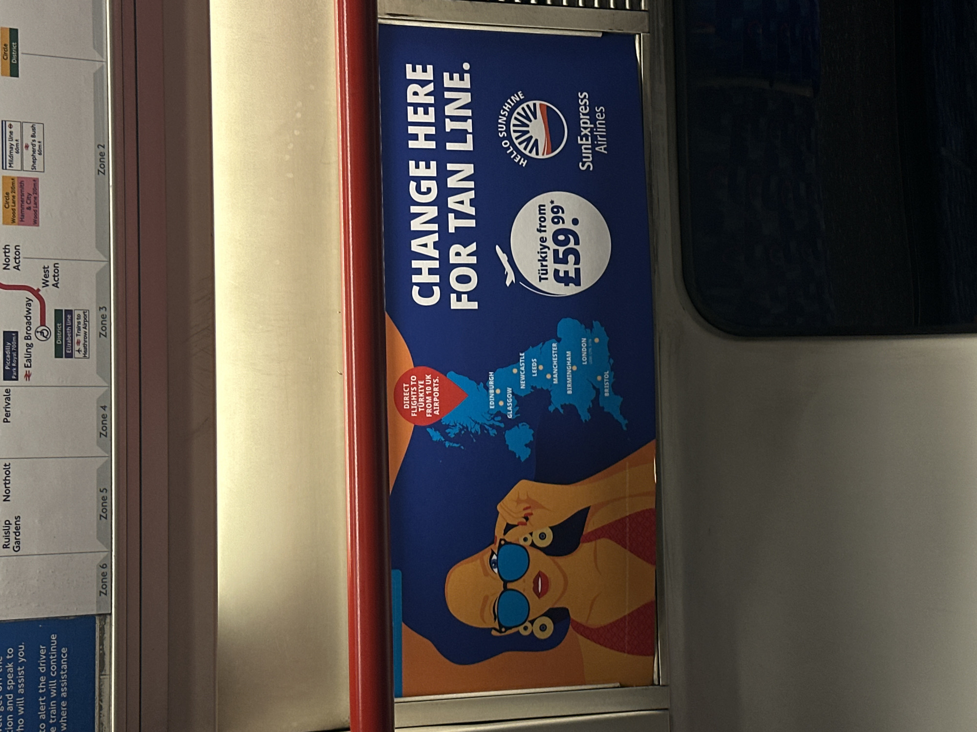 The image shows the interior of a London Underground train car. A map showing various stations and lines, including the Piccadilly Line, District Line, Elizabeth Line and Circle Line, indicates that the train is running between Zone 2 and Zone 6. An advertisement for SunExpress Airlines is posted on the train. It promotes flights to Turkey from £59.99 and features a woman wearing sunglasses.