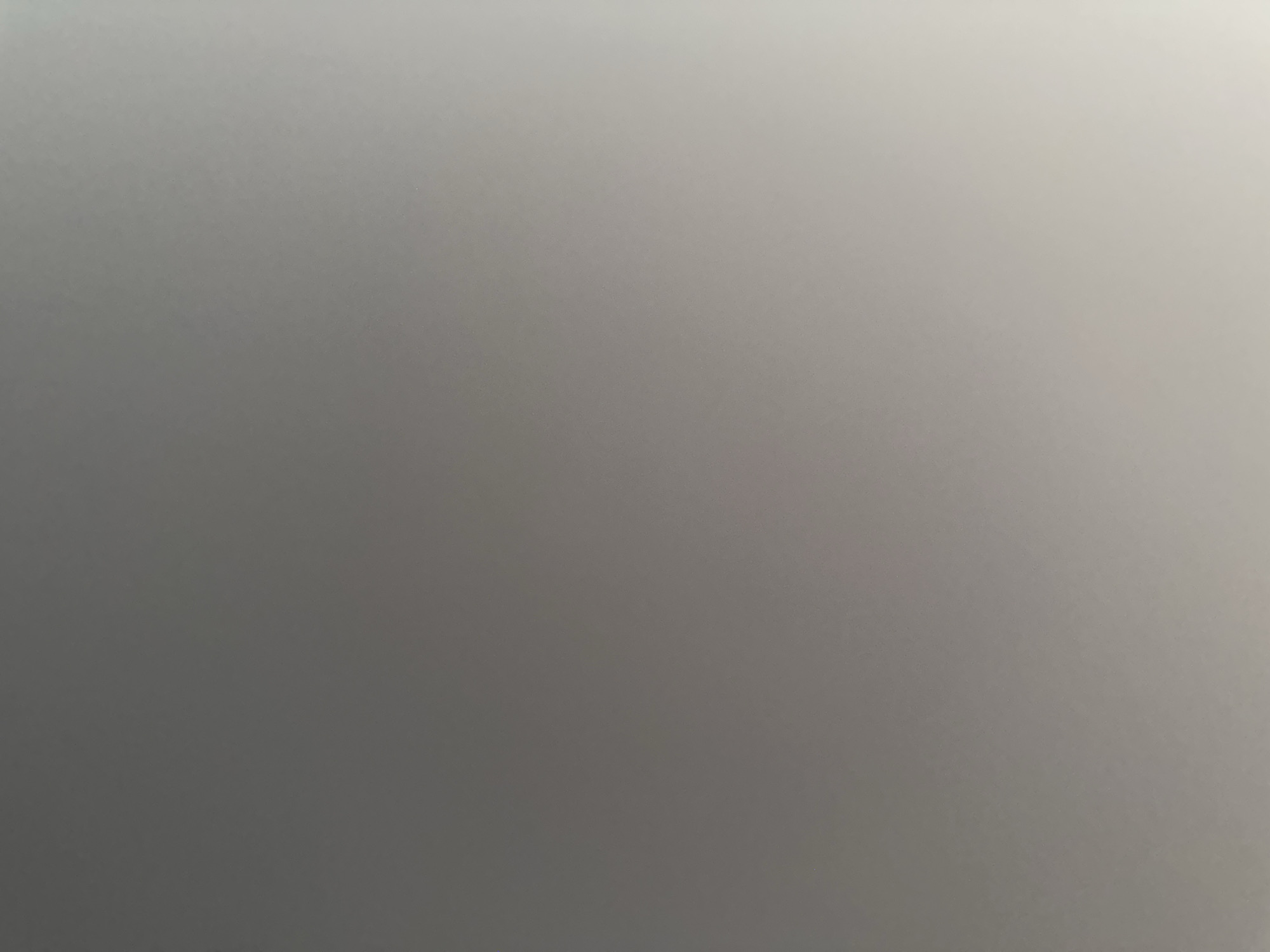 This is a close-up, abstract image with a smooth, gradient texture. The primary color is a neutral gray, transitioning from a darker shade on the left to a lighter, almost white shade on the right. The lighting creates a subtle gradient, suggesting a light source from the top right. There are no discernible subjects, objects, scenes, activities, or events depicted. The image is devoid of any text. The overall impression is one of minimalism and a lack of specific detail, making it difficult to ascertain any context related to time of day, weather, location, or emotions. The image appears to be a photograph of a plain, uniformly colored surface, possibly a wall, fabric, or a digitally generated texture.