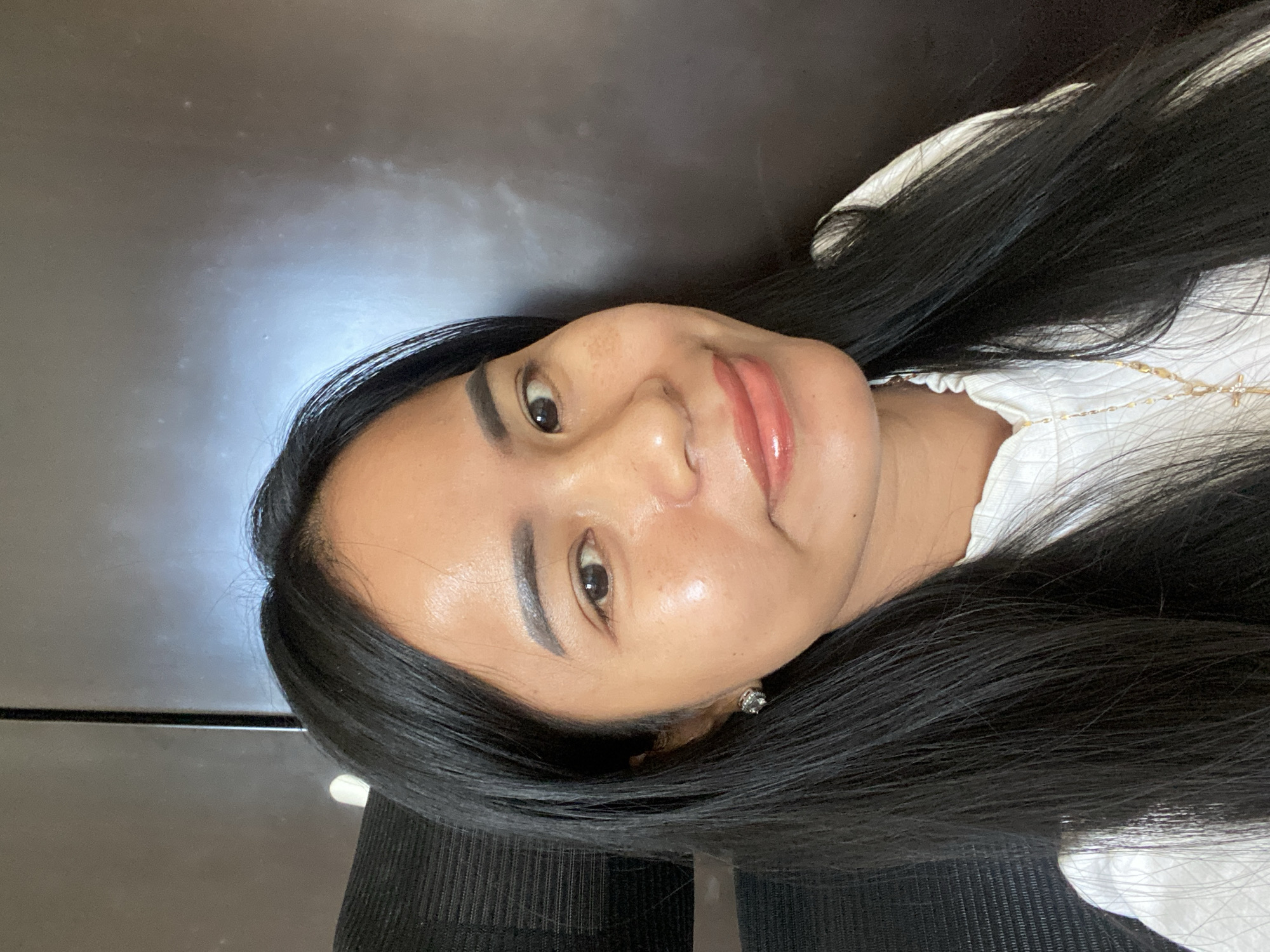 A person with black hair is facing the camera and smiling. They are wearing a white top and a necklace with a star pendant. The background appears to be a dark, possibly indoor, environment. There is no information to confirm the location in North Kuta, Indonesia.