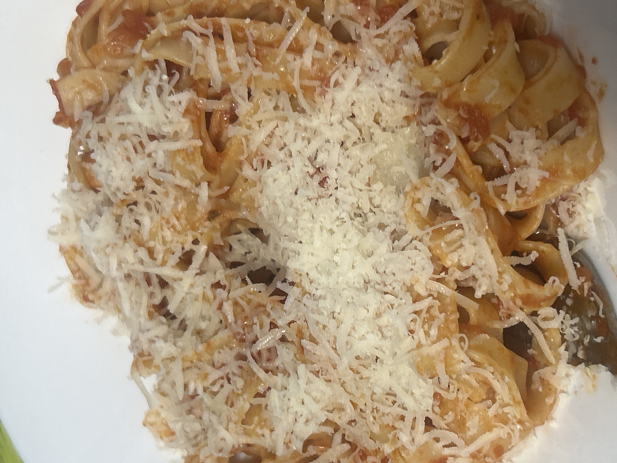 A close-up shot shows a plate of tagliatelle pasta covered in tomato sauce and grated cheese. The pasta appears to be freshly prepared, with a generous portion of cheese sprinkled on top. The focus is on the food, obscuring any environmental details that might suggest a specific location. There are no people visible in the image.