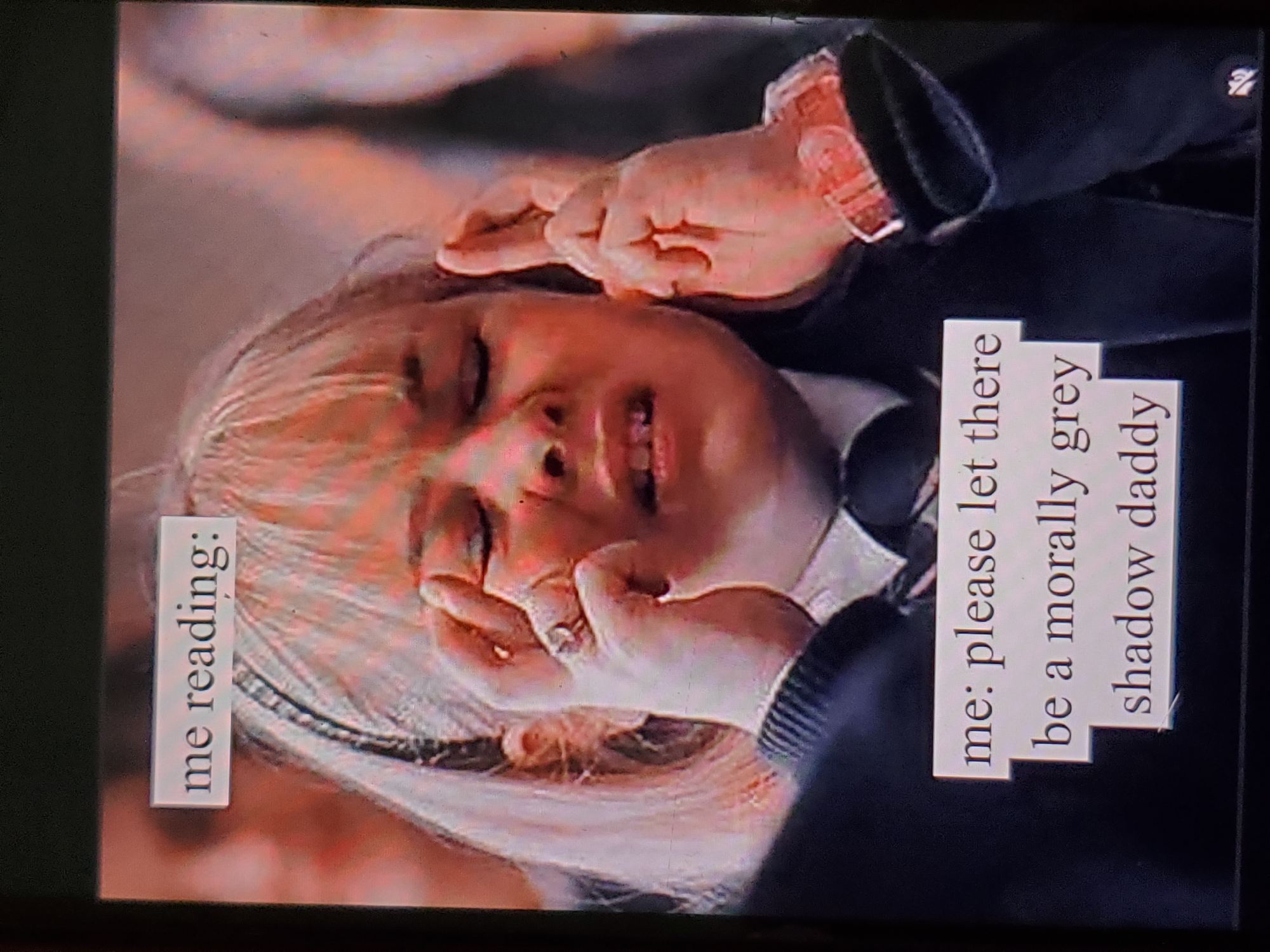 A close-up, slightly blurry, low-angle photograph captured on a screen shows a young Caucasian female with blonde hair and a pink watch on her left wrist. She is wearing a dark school uniform with a white collar and tie. The girl is sitting in what appears to be an auditorium or classroom, with other people visible in the blurred background. She has her eyes closed and is touching her temples with her fingers, conveying a sense of distress or intense thought. Overlay text in two rectangular boxes is visible: the top box reads "me reading:", and the bottom box contains multiple lines of text including "me: please let there be a morally grey shadow daddy". The image is overexposed in some areas, particularly on the girl's face.