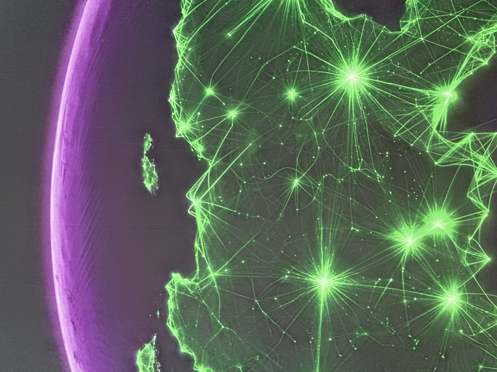 The image displays a stylized representation of a globe or planet, with a curved, purple-hued upper atmosphere or aurora. The surface is depicted with a dark, textured background, overlaid with a luminous green network of lines and nodes. These lines connect numerous points of light, creating a complex web that suggests a global network of some kind, possibly representing communication, transportation, or energy grids. The landmasses are vaguely outlined, with the bright green points and connecting lines signifying high activity or connection points. One prominent cluster of intensely bright, star-like points with radiating lines is visible in the lower right quadrant of the image, suggesting a major hub within this network. The overall aesthetic is abstract and technological, reminiscent of data visualization or a science fiction depiction of interconnectedness. There are no discernible people, specific objects, or actions within the image. The location of Norilsk, Russia, is not explicitly identifiable within this abstract visualization.