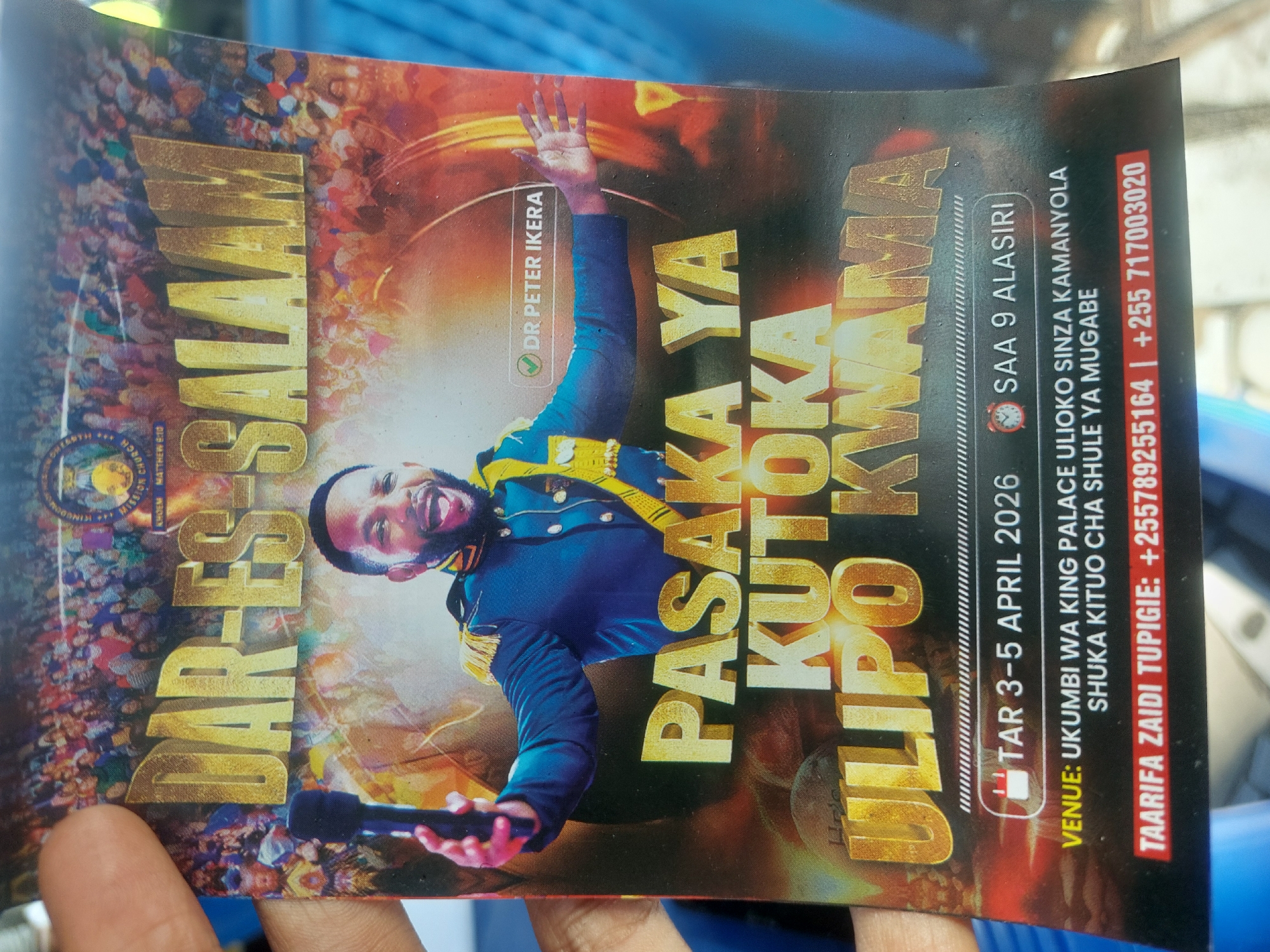 The image shows a flyer advertising a religious event in Dar es-Salaam, Tanzania. The event, titled "Pasaka Ya Kutoka Ulipo Kwama," featuring Dr. Peter Ikera, is scheduled for April 3-5, 2026, at 9 AM. The venue is Ukumbi wa King Palace in Sinza Kamanyola, near the Shule ya Mugabe bus stop. Contact numbers for information are listed. The flyer features a photo of a man in a blue military-style jacket, holding a microphone, superimposed over a crowd. The Dar-es-Salaam name is prominent.