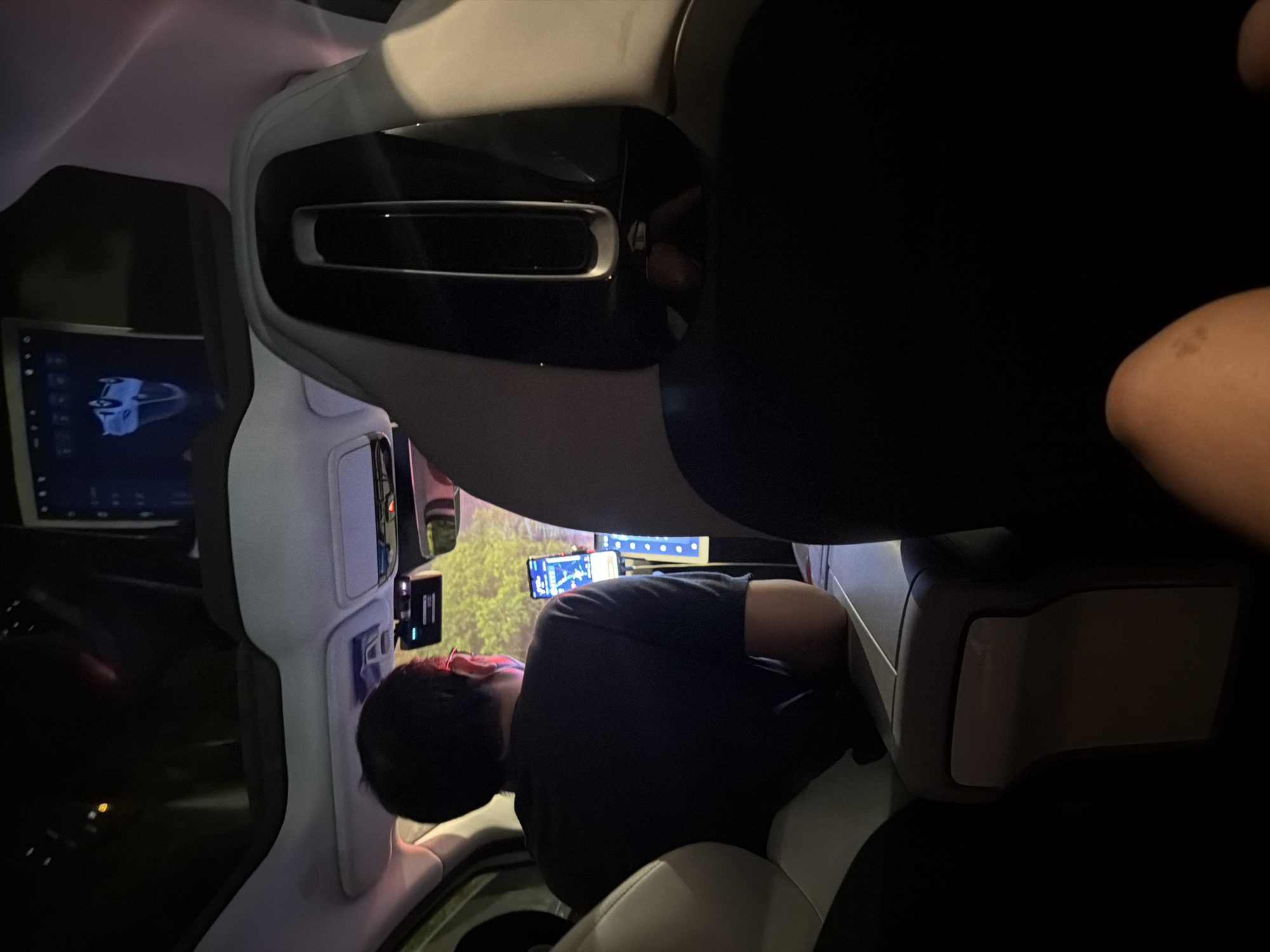 A person is seated in the passenger seat of a car. The person is wearing a dark-colored shirt, and is looking towards a dashboard screen. A screen is also located to their left. The interior of the car is primarily shades of gray and black. The location of the image is in Yuhuatai District, China.