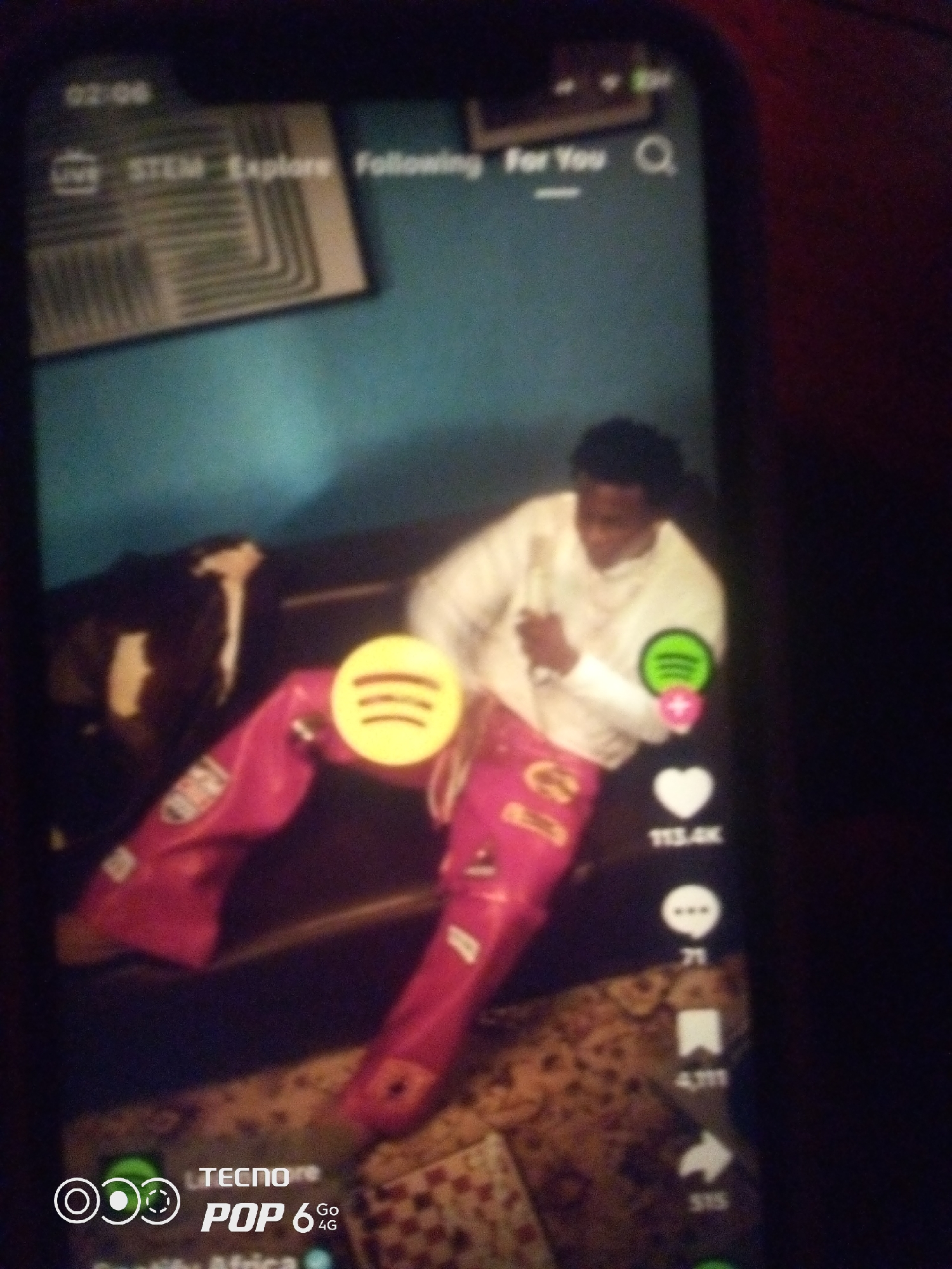 The image shows a person in the city of Howayi, Nigeria. The person is wearing pink pants and a white shirt, and they are sitting on a couch. There is a Spotify logo on the person's pants, and a heart icon with the number 113.4K next to it. The overall scene appears to be a casual indoor setting.