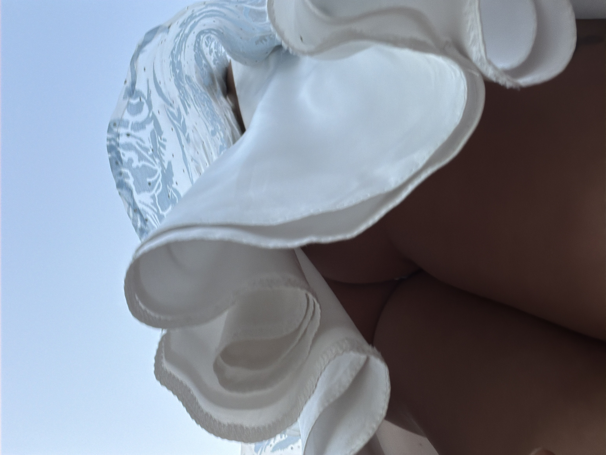 The image shows a low-angle shot of a person's legs and a white skirt caught in the wind. The skirt is white with a light blue floral pattern. The background is a clear sky. The image does not contain any information about a specific location in Bila Tserkva, Ukraine.