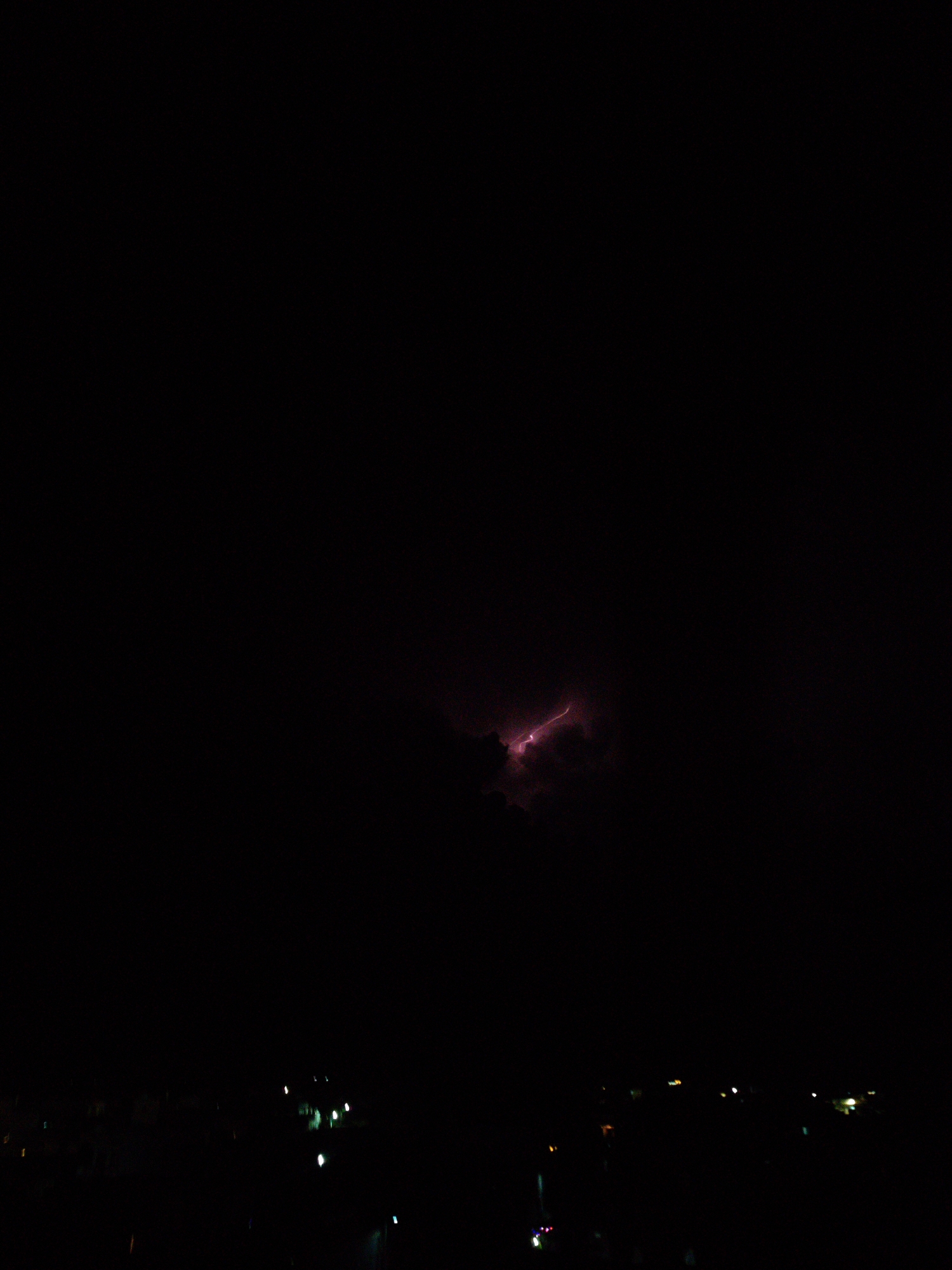 The image shows a nighttime scene in Phú Quý Special Administrative Region, Vietnam, featuring a lightning strike illuminating a patch of clouds in the otherwise dark sky. Below the clouds, there are faint lights suggesting a cityscape.