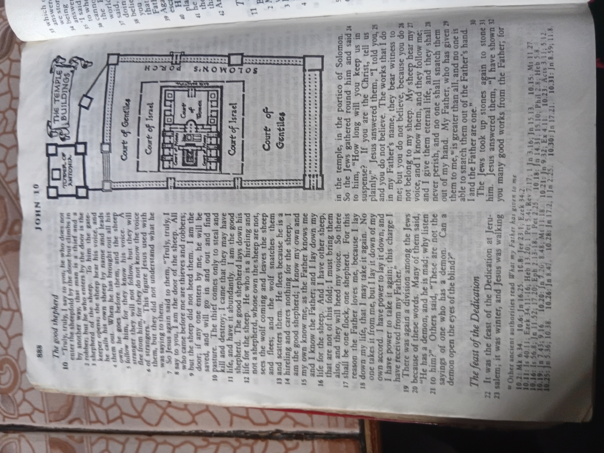 This media file contains an image of an open Bible, with text from the Gospel of John, chapter 10, visible on the pages. The text discusses Jesus as the good shepherd and includes a diagram of the Temple in Jerusalem. There is also a small illustration of the Tower of Antonia. The pages of the Bible are slightly worn, indicating use. The overall setting appears to be indoors, likely a room with natural light. The light source seems to be coming from the right side of the image, illuminating the text and diagram. The context provided, "Nkpor, Nigeria," suggests that this Bible is located in that region, though there are no explicit visual cues within the image itself to confirm this specific location. The text focuses on biblical passages and a historical diagram, with no discernible human subjects or active events taking place within the frame of the image. The visible text is in English and includes chapter and verse numbers, as well as headings like "The good shepherd" and "The feast of the Dedication."