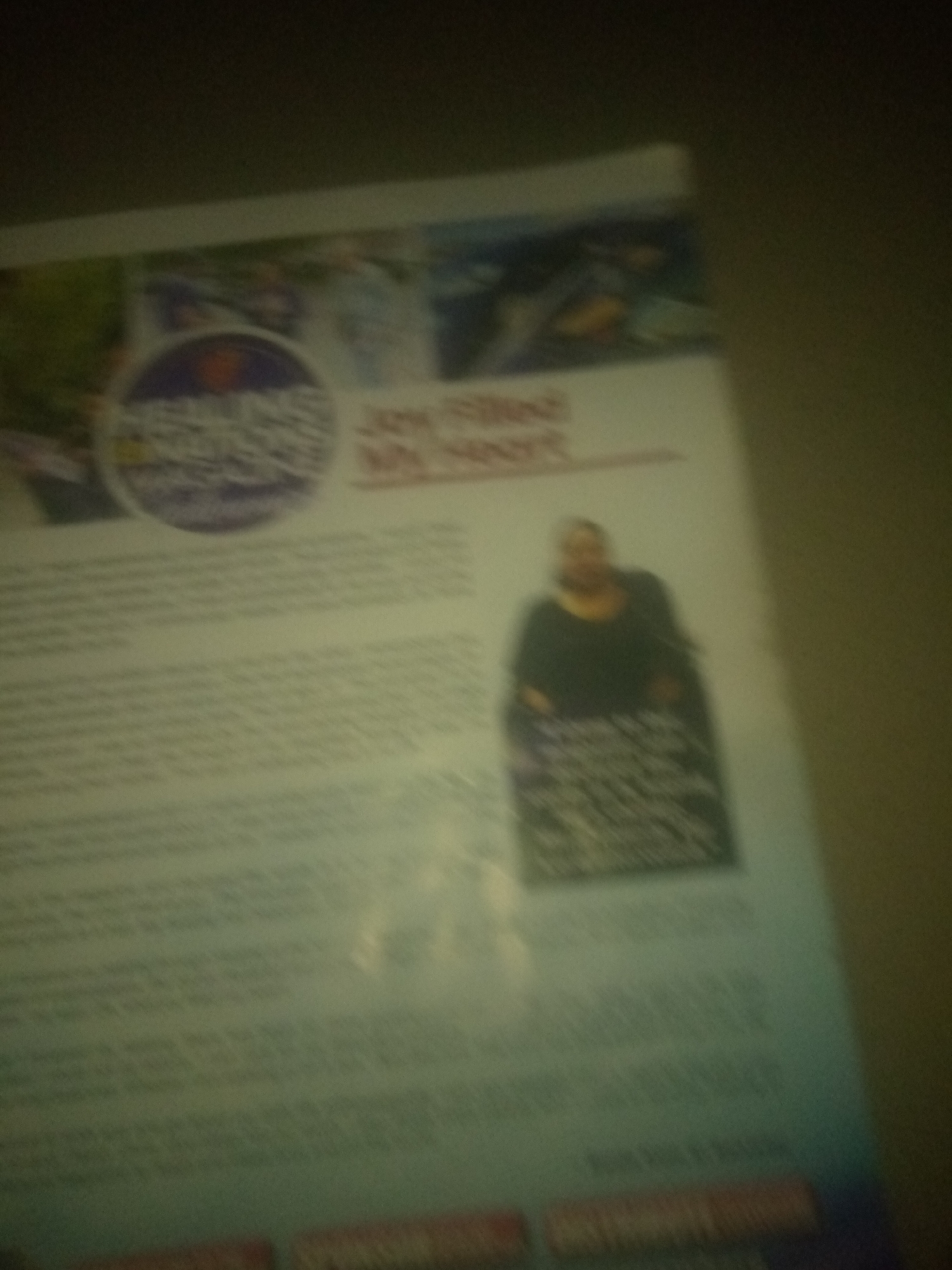 The image shows a blurry book or magazine with text and images. In the upper left, there is a circular logo with some text inside. To the right of the logo, there is text that appears to read "Joy Filled My Heart". Below this, there is a blurry image of a woman sitting in a chair, wearing a dark top and a patterned skirt. The background of the page is mostly white with some text printed on it. The overall image is out of focus and it is not possible to identify the location in Jauro Yinu, Nigeria, or any specific details about the contents beyond what is visible.