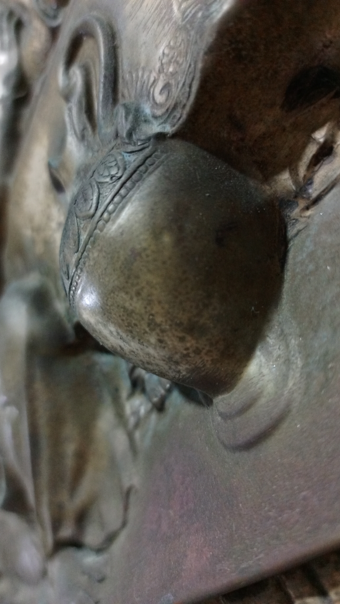 A close-up shot depicts a textured, metallic object, likely part of a larger sculptural piece. An ornate band encircles a rounded element, suggesting decorative carving. The overall material appears aged or patinated. It does not provide information about a location or the existence of people, subjects, or actions in the city of Los Robles, Venezuela.