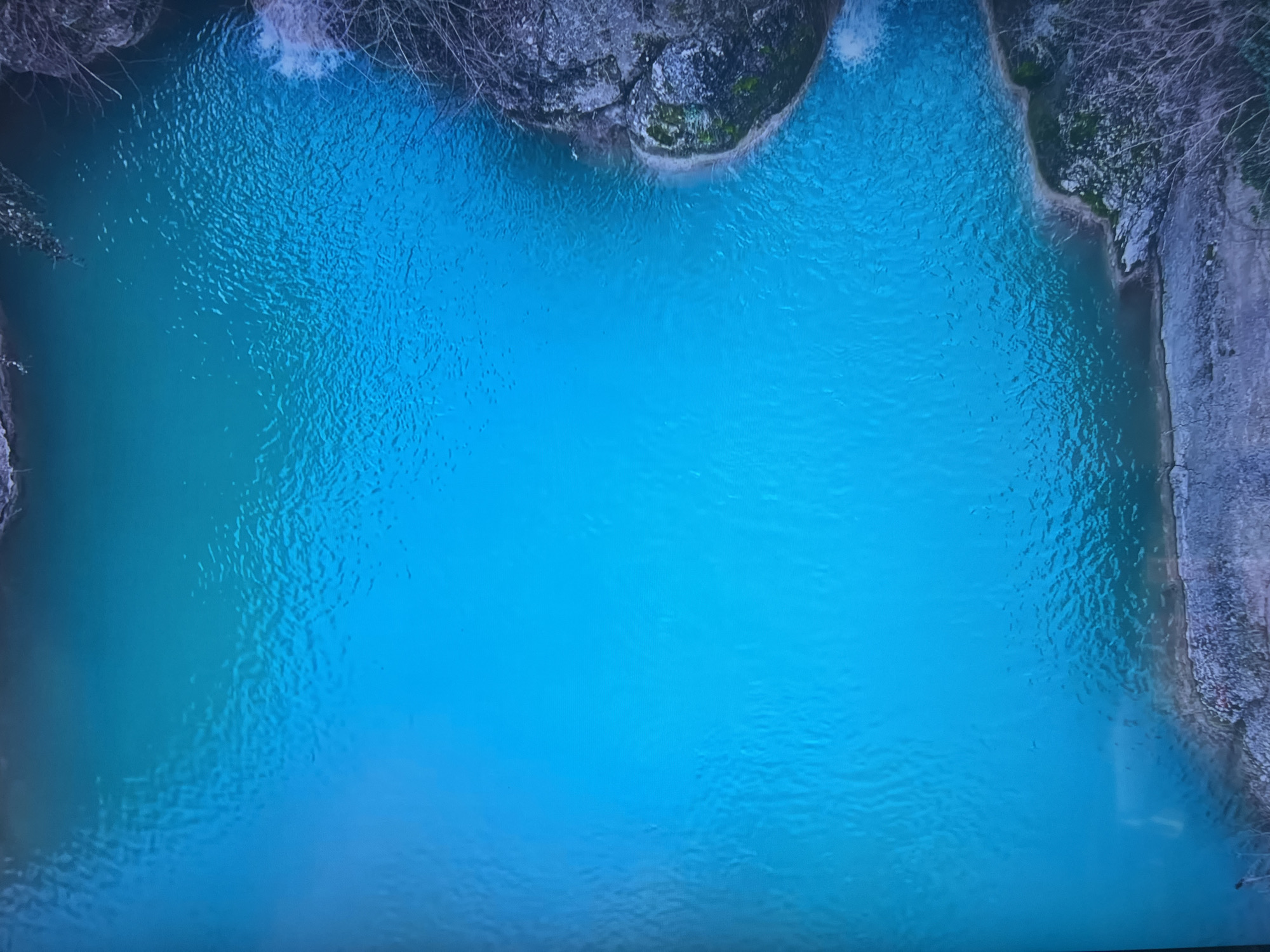 The image depicts a body of turquoise water surrounded by rocky cliffs with some vegetation. The water surface is rippled. Bare tree branches are visible along the cliff edges. The location is not discernible from the image alone. Therefore, it is not possible to confirm its location within Basingstoke and Deane, United Kingdom.