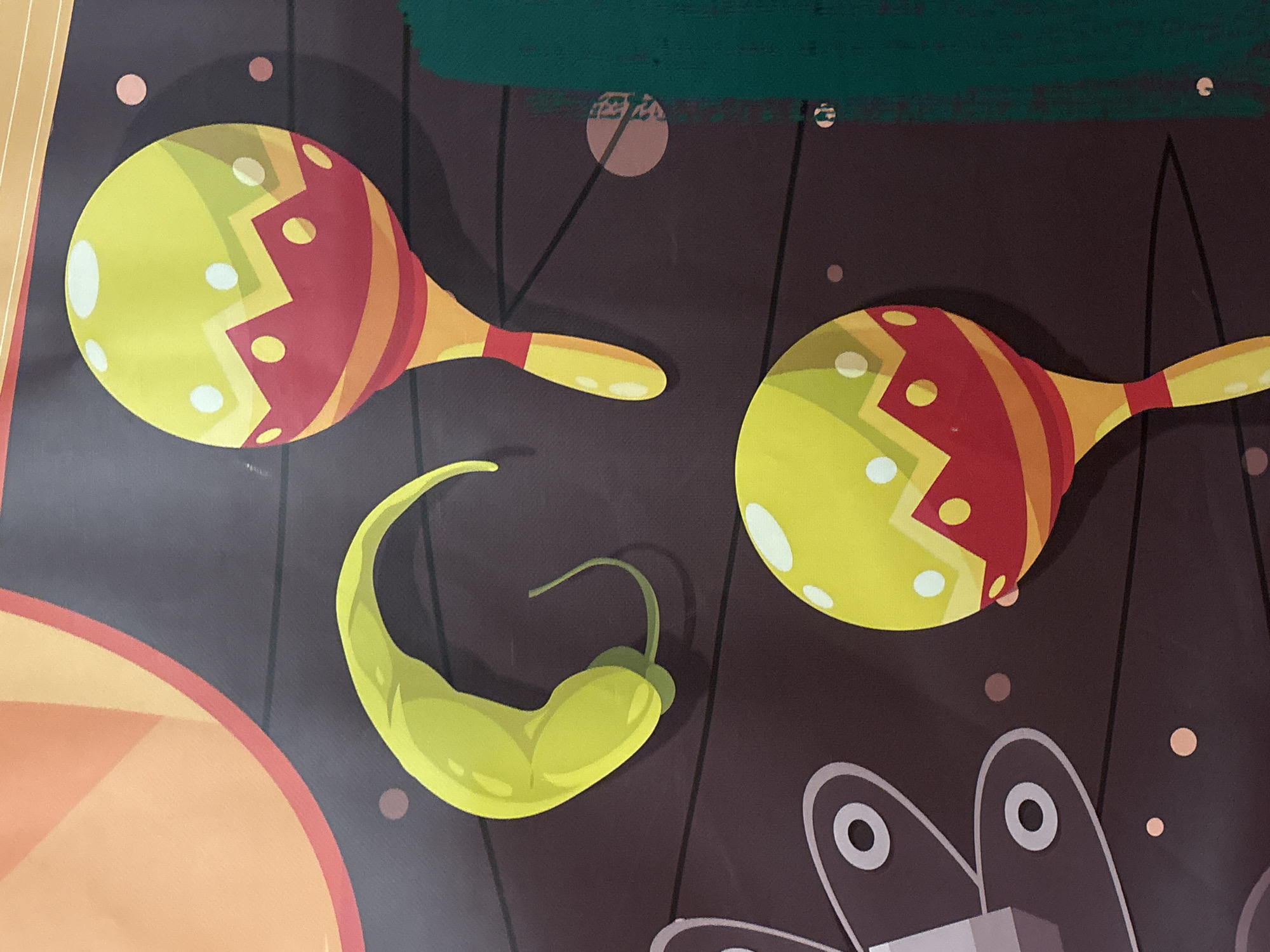 The image displays a colorful illustration featuring two maracas and a green chili pepper. The maracas are predominantly yellow with red and orange accents and white circular dots. The chili pepper is a vibrant green and has a curved shape. The background is a dark brown, textured surface with thin black lines and a few scattered dots of pink and orange. A section of an orange and pink circular shape is visible in the upper left corner, and a textured green vertical strip is present on the right side. There are no people or specific identifiable landmarks present in the image, making it impossible to determine its location in Dubai or the United Arab Emirates.