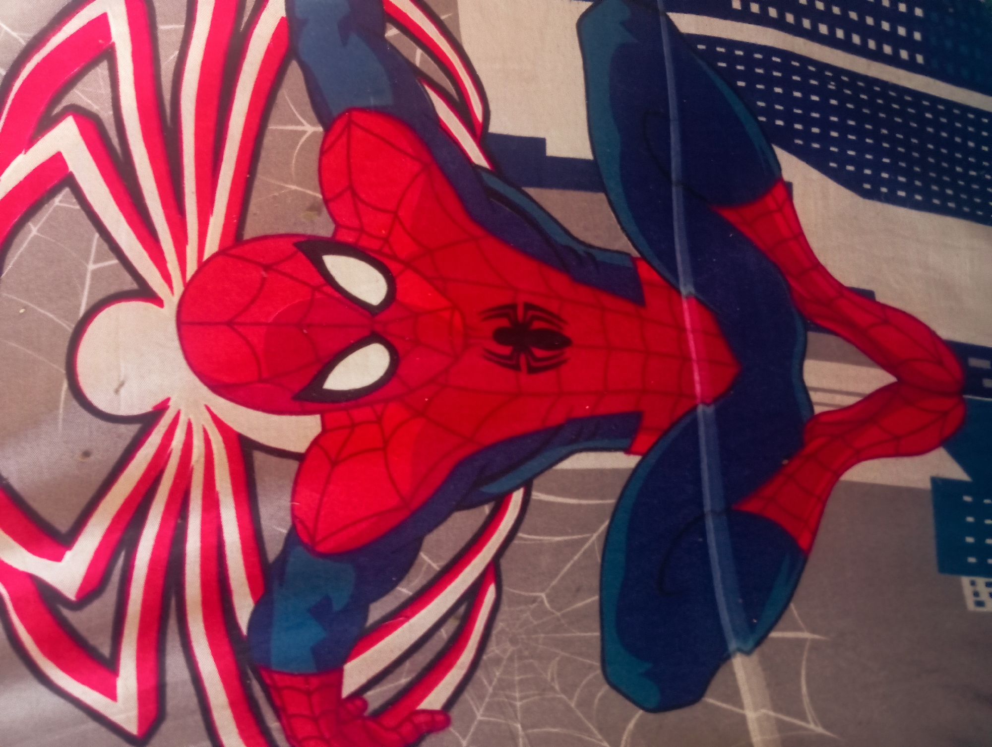 The image depicts a Spiderman-themed object, possibly bedding or fabric. The design features Spiderman in a dynamic pose against a background that includes elements like spiderwebs and what appears to be a cityscape. The colors are predominantly red, blue, and grey. The image's location within the city of Nkpor, Nigeria is not discernible from visual evidence alone.