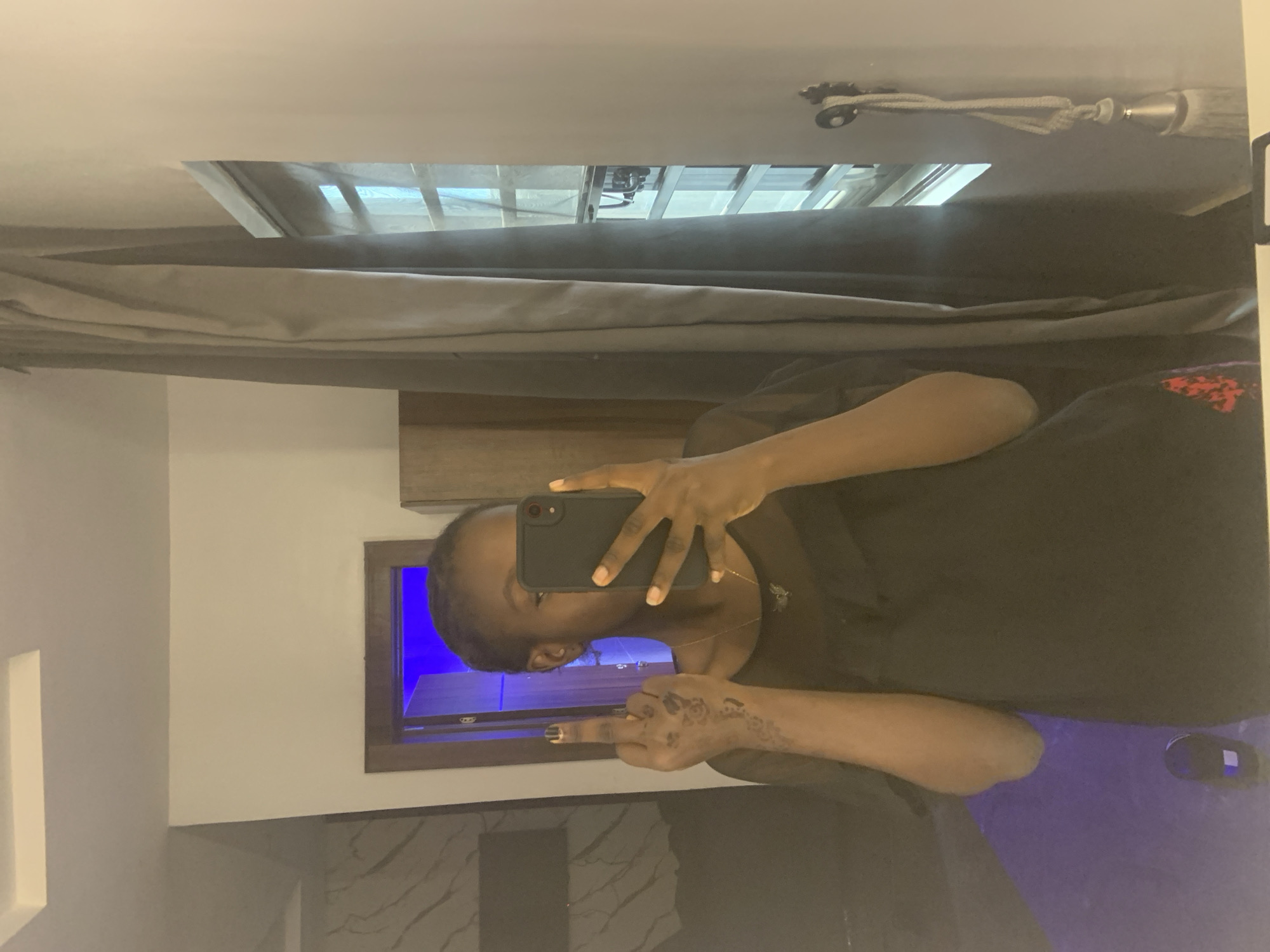 A person is taking a mirror selfie. The background shows a room with a television mounted on the wall. The specific location and city of Ota, Nigeria, cannot be determined from the image. The person's middle finger is raised.
