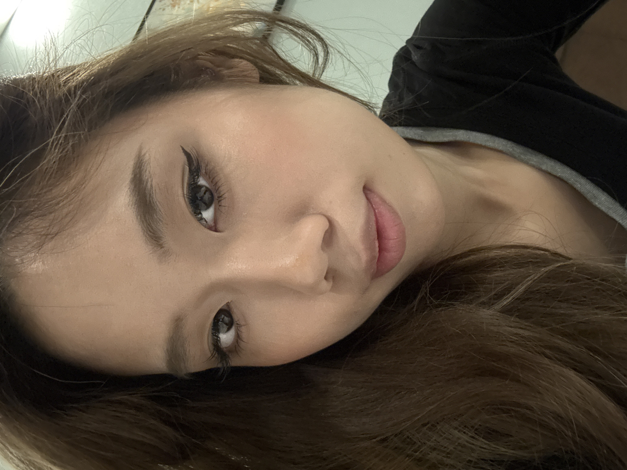 A close-up, angled view shows a woman's face. She has light skin, dark eyeliner, and long brown hair. She wears a black top with a gray neckline. There is no information in the image to suggest that this image was taken in Lanzhou, China.