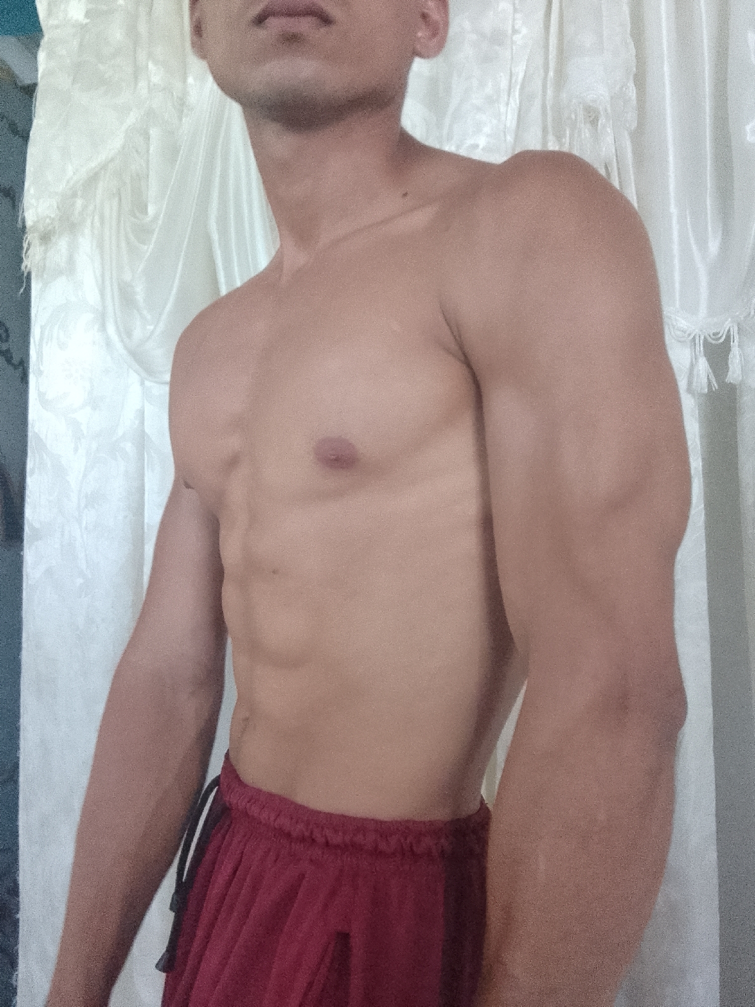A shirtless man is indoors, wearing red shorts. He is standing against a white curtain. The location is unknown, and there's no evidence of Juan Griego, Venezuela.