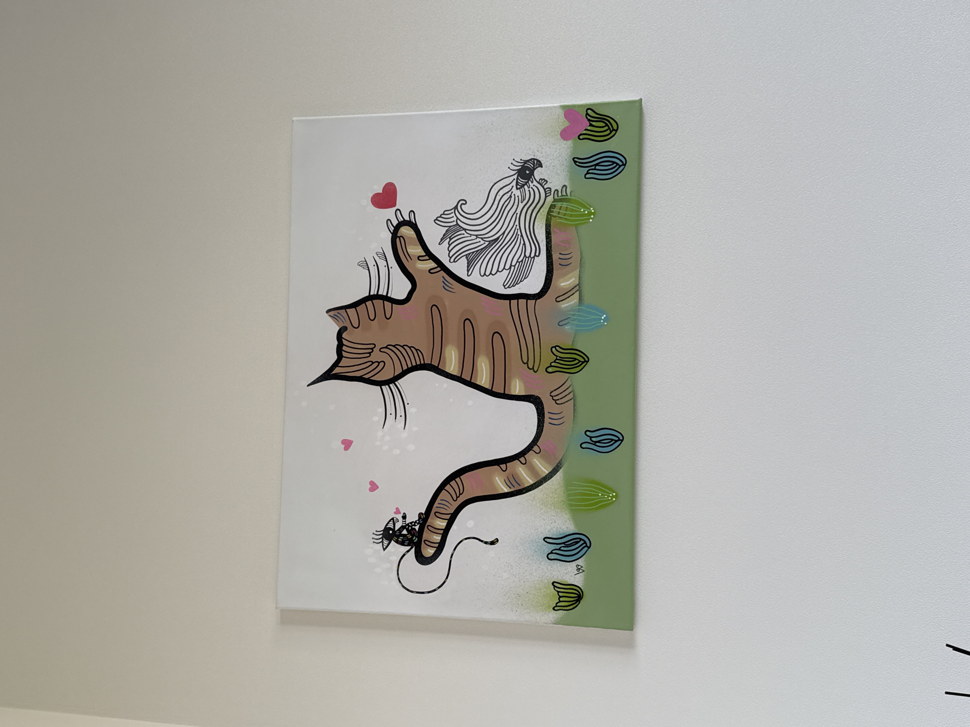 The image shows a painting hanging on a white wall. The painting depicts a stylized cat with brown and black stripes, in a curved, almost question-mark shape. On the cat's back sits a drawn bird with lots of feathers, and a small mouse is drawn at the tail. There are several hand painted symbols down the side of the painting, and two hearts are shown by the cat's head. The background of the painting is white, except for the far right of the painting which is light green. There are no people or identifiable landmarks visible in the image. There's no indication that the picture was taken in Sochi, Russia.