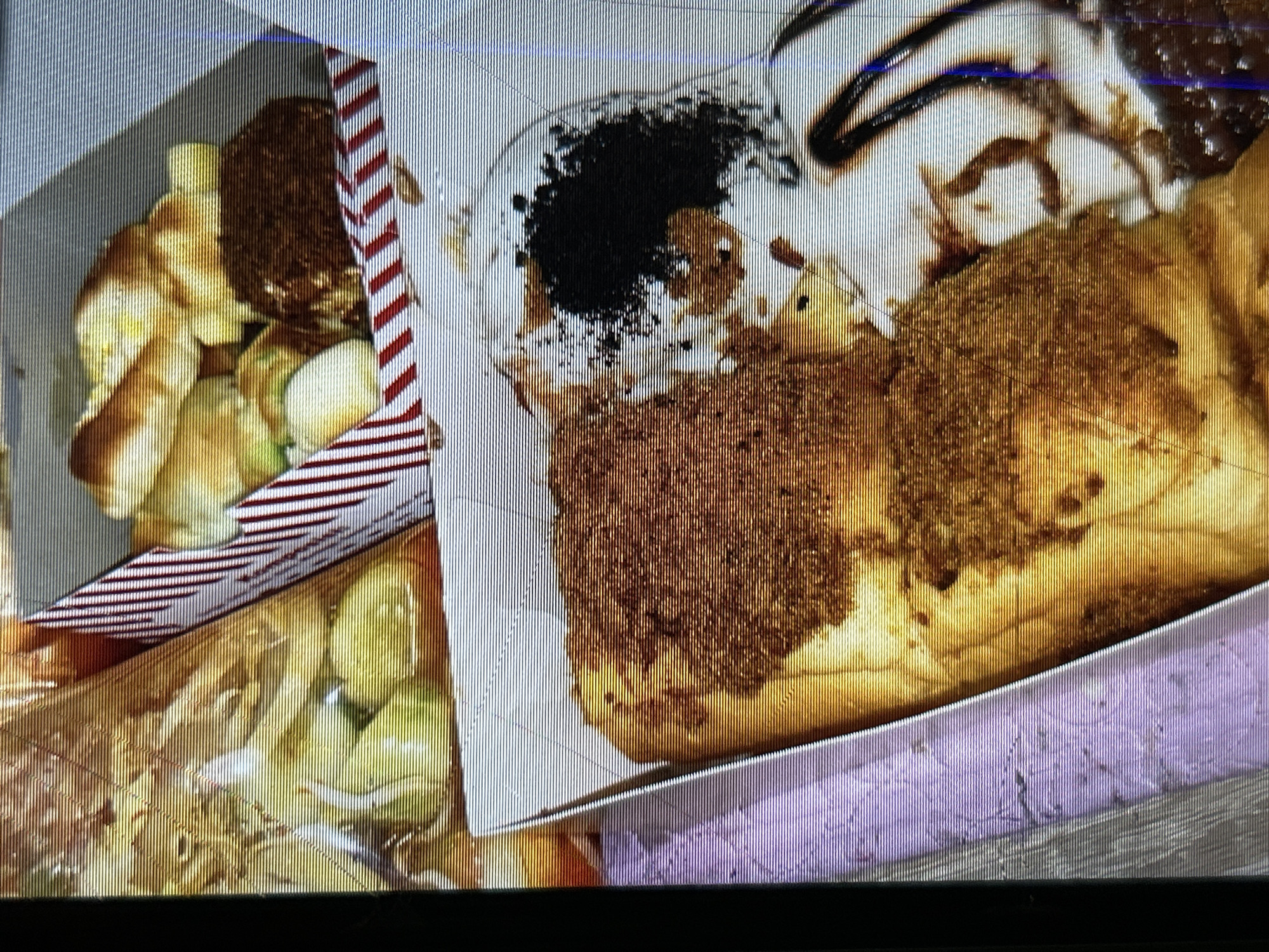 The image shows a close-up view of several baked goods presented in paper containers. In the foreground, a large pastry is topped with a generous amount of a dark, crumbly seasoning. To its right, a portion of a white pastry is visible, adorned with chocolate sauce and a scattering of dark, granular material. In the background, another container holds several smaller, golden-brown pastries, some appearing to have a glossy finish. The overall presentation suggests a bakery or a food stall. The image is taken from a slightly elevated angle, focusing on the textures and details of the baked items. The context of Depok, Indonesia is not visually ascertainable from the provided image.