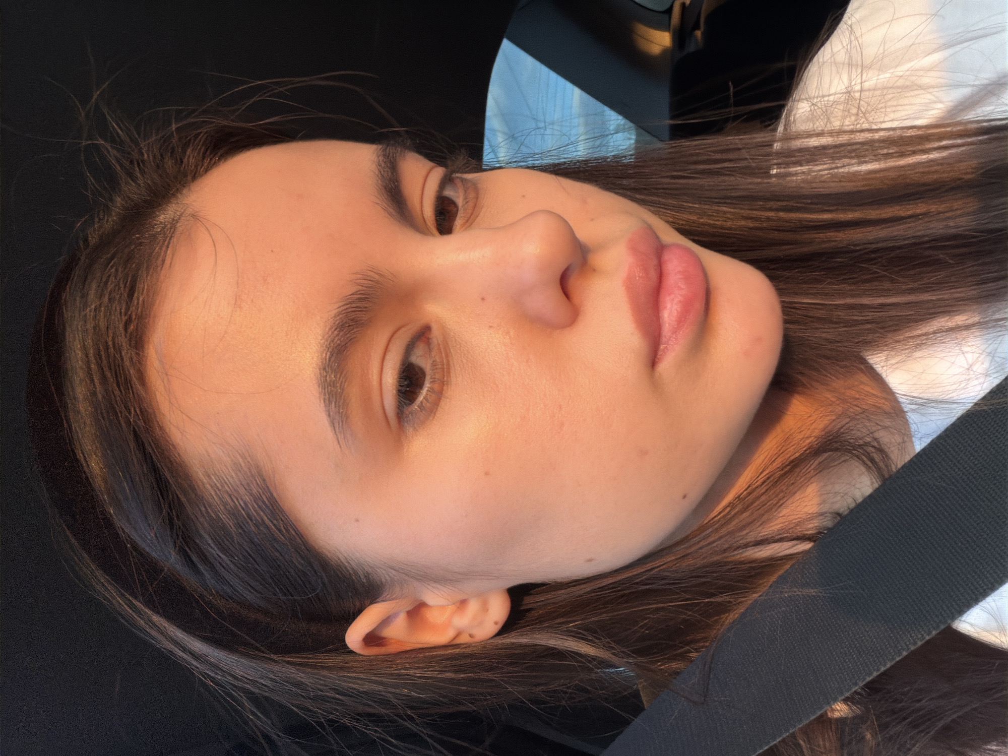 A close-up selfie shows a young woman with brown hair and fair skin. She has dark eyebrows and brown eyes. She is wearing a seatbelt, suggesting she is in a car. The location cannot be determined from the image. The city of Chaikovsky, Russia, is not visible in the image.