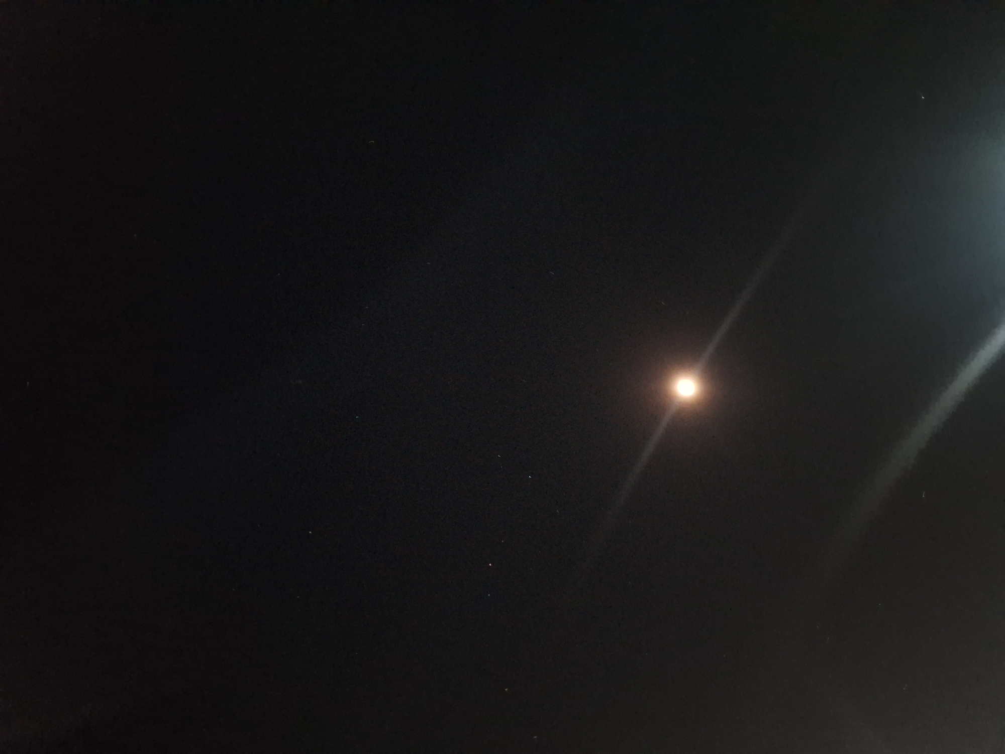 The image is a dark, wide-angle shot of the night sky. A bright, circular light source, possibly the moon or a strong street lamp, is visible in the lower right quadrant, casting a prominent beam of light diagonally across the frame. Several small, faint dots, likely stars, are scattered across the dark expanse of the sky. The overall impression is of a clear night with a single, bright celestial or artificial light source. The location is identified as Samarinda, Indonesia.