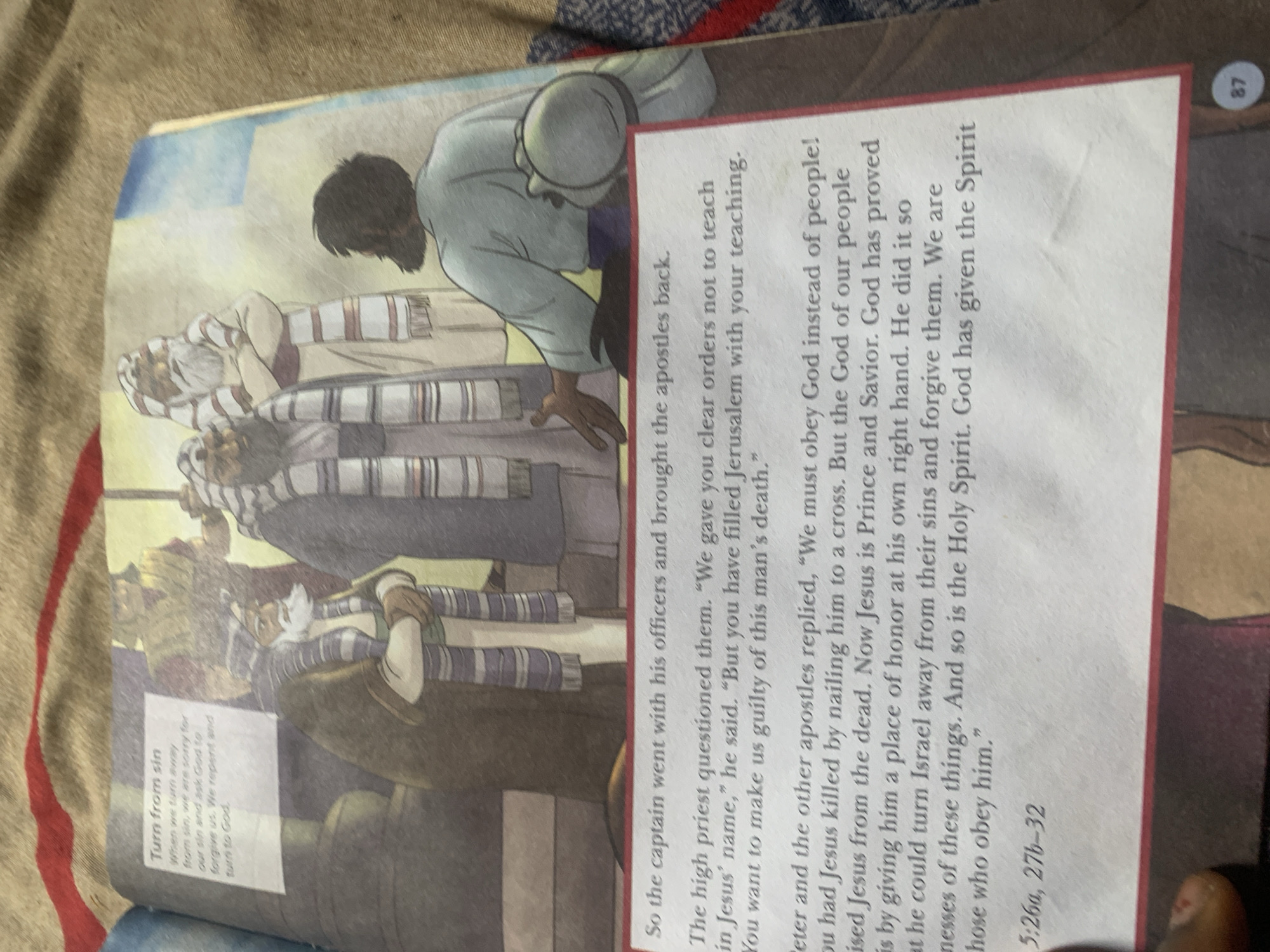 The image shows an open book with text and an illustration. The illustration depicts three men in religious attire, with two facing the viewer and one with his back to the viewer. They are standing in what appears to be an outdoor setting, possibly ancient.
The text on the left side of the book, under the heading "Turn from sin," discusses repentance and seeking forgiveness from God. The main body of the text describes a scene where the high priest questions individuals, and Peter and other apostles respond, referencing Jesus and his resurrection. The text also mentions obedience to God and the Holy Spirit. A scripture reference, "5:26a, 27b-32," is visible at the bottom left.
The page number "87" is visible on the bottom right of the book. The background of the image is a textured fabric, likely a blanket or tablecloth. The scene described in the text is not set in a specific city like Jauro Yinu, Nigeria, but rather appears to be a biblical narrative.