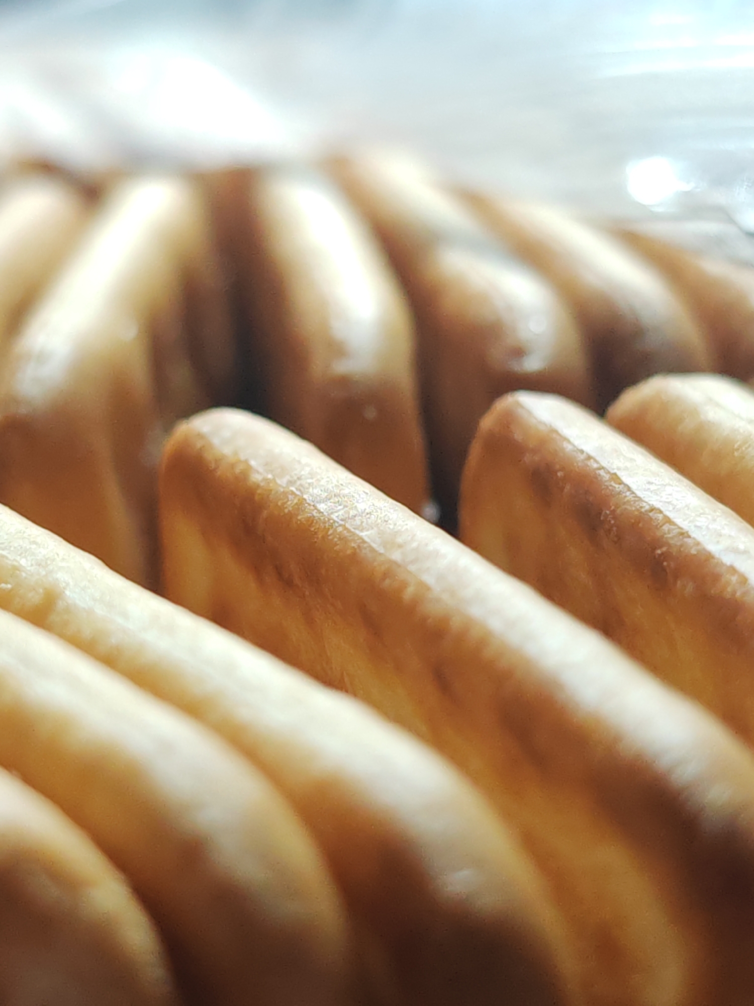 A close-up image shows rows of breadsticks. The breadsticks are arranged in neat rows, with the focus on the front rows, which are lighter in color. The rows towards the back of the image are slightly out of focus and appear darker. The lighting creates highlights and shadows, emphasizing the texture of the breadsticks. The context of Hrodna, Belarus is not clear from the image itself.