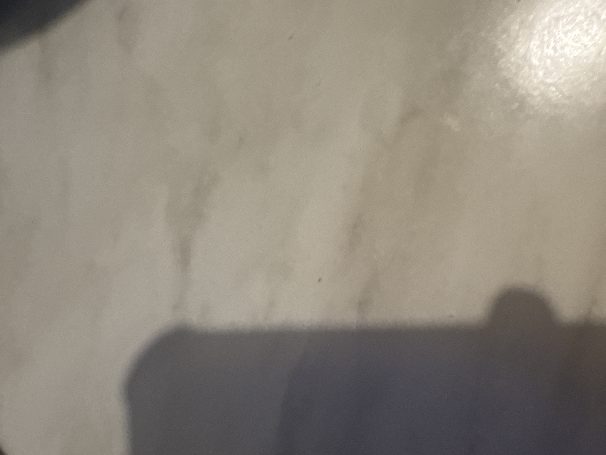 The image shows a close-up of a light-colored surface with a dark shadow cast upon it. The surface appears smooth with subtle variations in texture and a slight sheen in the upper right corner. The shadow is located in the lower right corner of the image. There is no visible indication of the location being Mexico City, Mexico. There are no people, subjects, objects, actions, or interactions visible in the image.