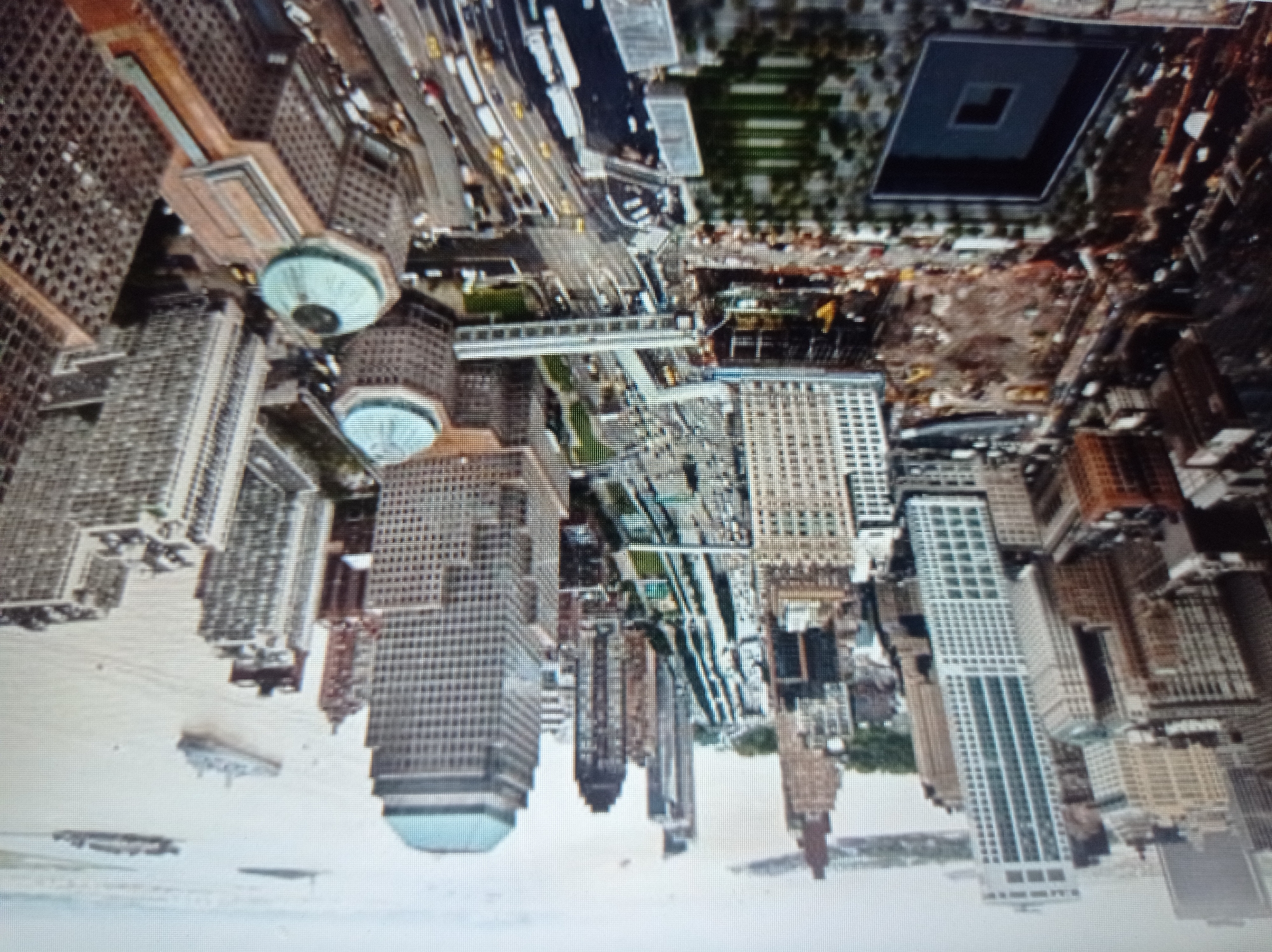 This is an aerial view of the National September 11 Memorial & Museum in New York City. The memorial features two large reflecting pools in the footprints of the Twin Towers, surrounded by trees. Nearby, skyscrapers dominate the skyline, and a highway passes through the scene. In the distance, boats are visible on the water. The image is taken from a high vantage point, capturing the urban landscape and the memorial. There is no indication of the city of Mukachevo, Ukraine in this image.