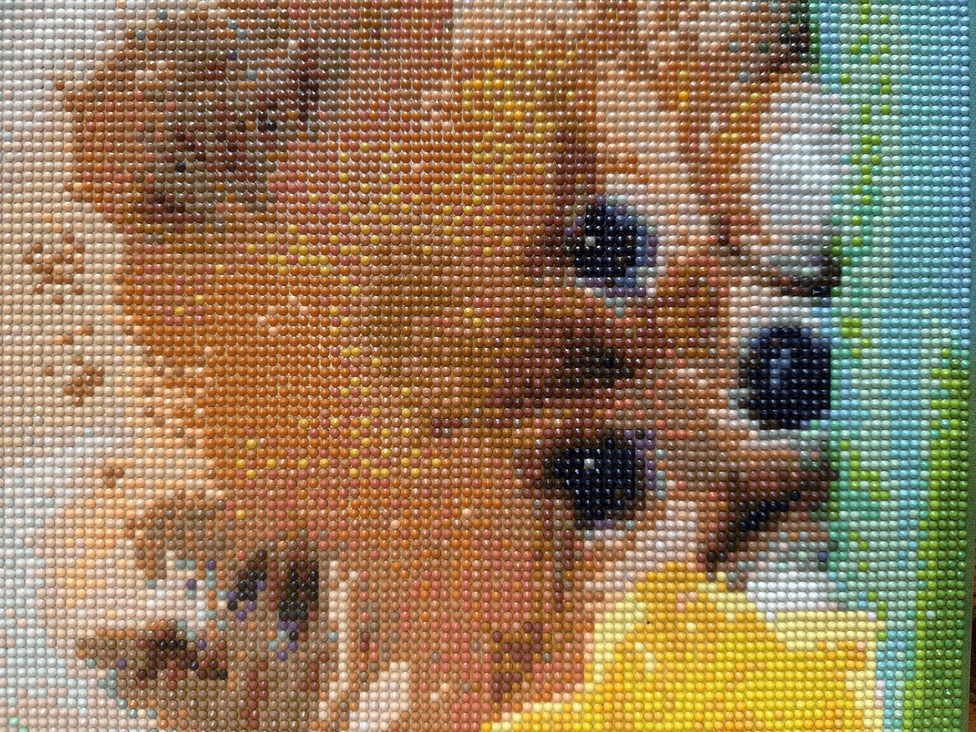 A close-up view of a diamond painting depicting a brown-haired animal with dark eyes. The diamonds are primarily shades of brown, tan, white, yellow, green and blue, creating a mosaic-like image. The animal is partially visible, with the focus on its eyes and surrounding fur. The location is Unknown, Unknown.