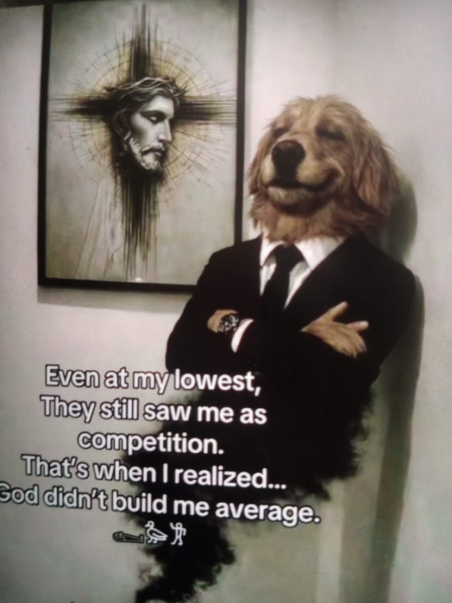 The image displays a humorous meme featuring a dog's head superimposed on a human body wearing a suit. Behind the dog-suited figure is a framed artwork depicting Jesus Christ wearing a crown of thorns, set against a radiating cross. The text overlay reads: "Even at my lowest, They still saw me as competition. That's when I realized... God didn't build me average." The composition suggests a playful juxtaposition of religious imagery and modern internet culture. There is no indication of this image being located in Jalingo, Nigeria, or any specific city.