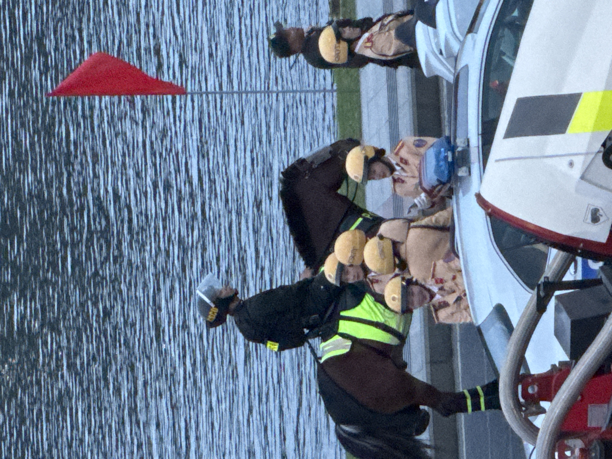 The image depicts a group of people, some of whom appear to be police officers on horseback, alongside a white vehicle that resembles an emergency response vehicle or a specialized transport. The setting seems to be near a body of water, possibly a lake or river, given the textured surface and reflections. The water has a rippled appearance, suggesting a calm or slightly breezy day.
Several individuals are wearing helmets and what appear to be tactical vests in bright green and yellow, commonly associated with safety or law enforcement personnel. One person is on horseback, wearing a dark uniform and a helmet, with the horse partially visible. The horse has a dark brown coat. The other individuals are standing near the white vehicle. The vehicle itself has a sleek design and visible emergency lights or markings, including yellow and red stripes. A red triangular flag is also visible in the upper left portion of the image.
The overall impression is that of an organized event or operation, possibly involving crowd control, a parade, or a public safety exercise. The lighting suggests it could be daytime, but the specific time of day is not clearly indicated. There are no strong emotional cues visible, as the faces of the individuals are not clearly discernible or are partially obscured. The location context of Da Lat, Vietnam, is provided, but no specific landmarks within the image clearly identify this location. Some text is visible on the vests of the officers, but it is too small and blurry to be deciphered.