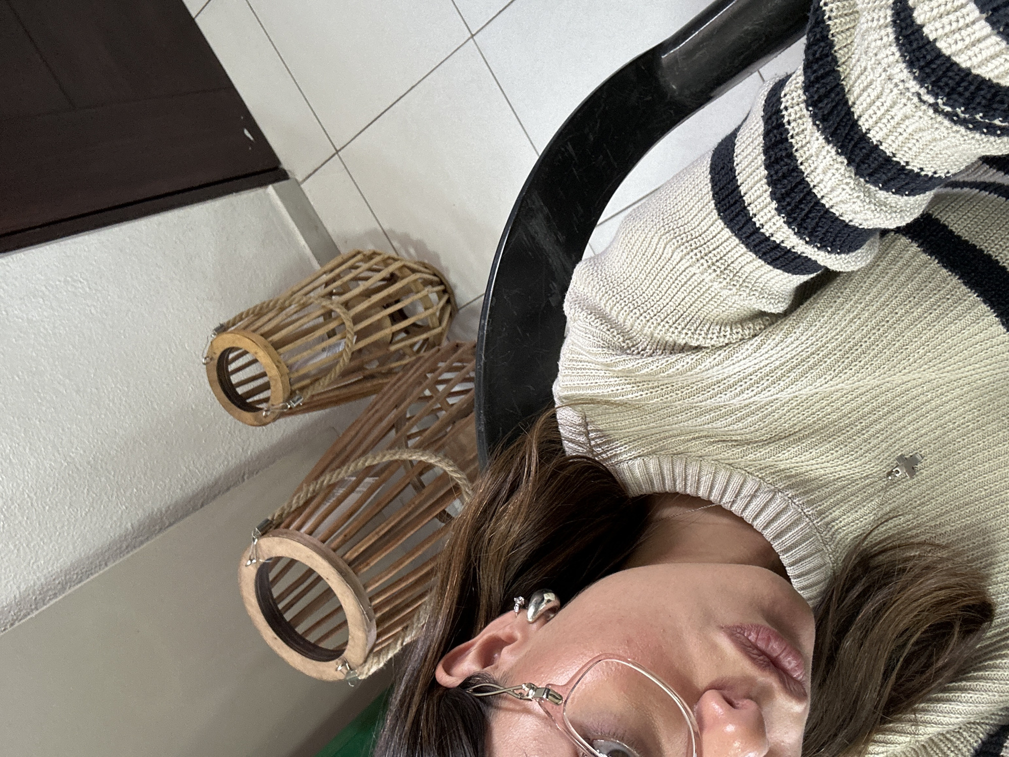 A high-angle shot shows a person in a black chair wearing a striped sweater, with two empty wicker lanterns on the floor. The location is Unknown, Unknown.