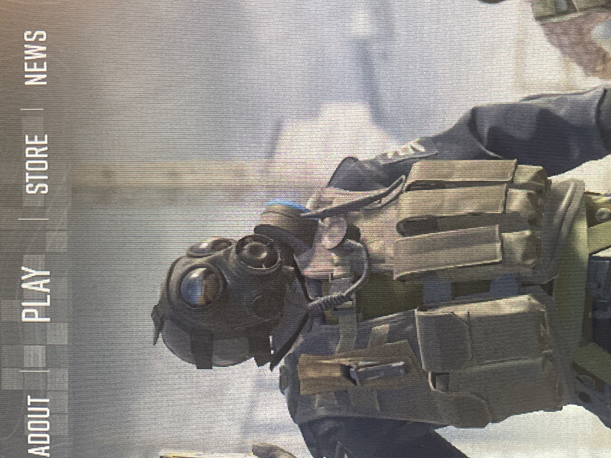 The image shows a close-up of a video game character wearing a gas mask and tactical gear. The character is standing in front of a blurred background that appears to be a desert or battlefield. The game's menu options, "ABOUT", "PLAY", "STORE", and "NEWS", are visible at the top of the screen. The character is a soldier with a dark uniform and a beige tactical vest with multiple pouches and straps. The gas mask is black with large, circular lenses. The lighting is diffused, suggesting an outdoor environment. The image quality is moderate, with visible pixelation and scan lines.